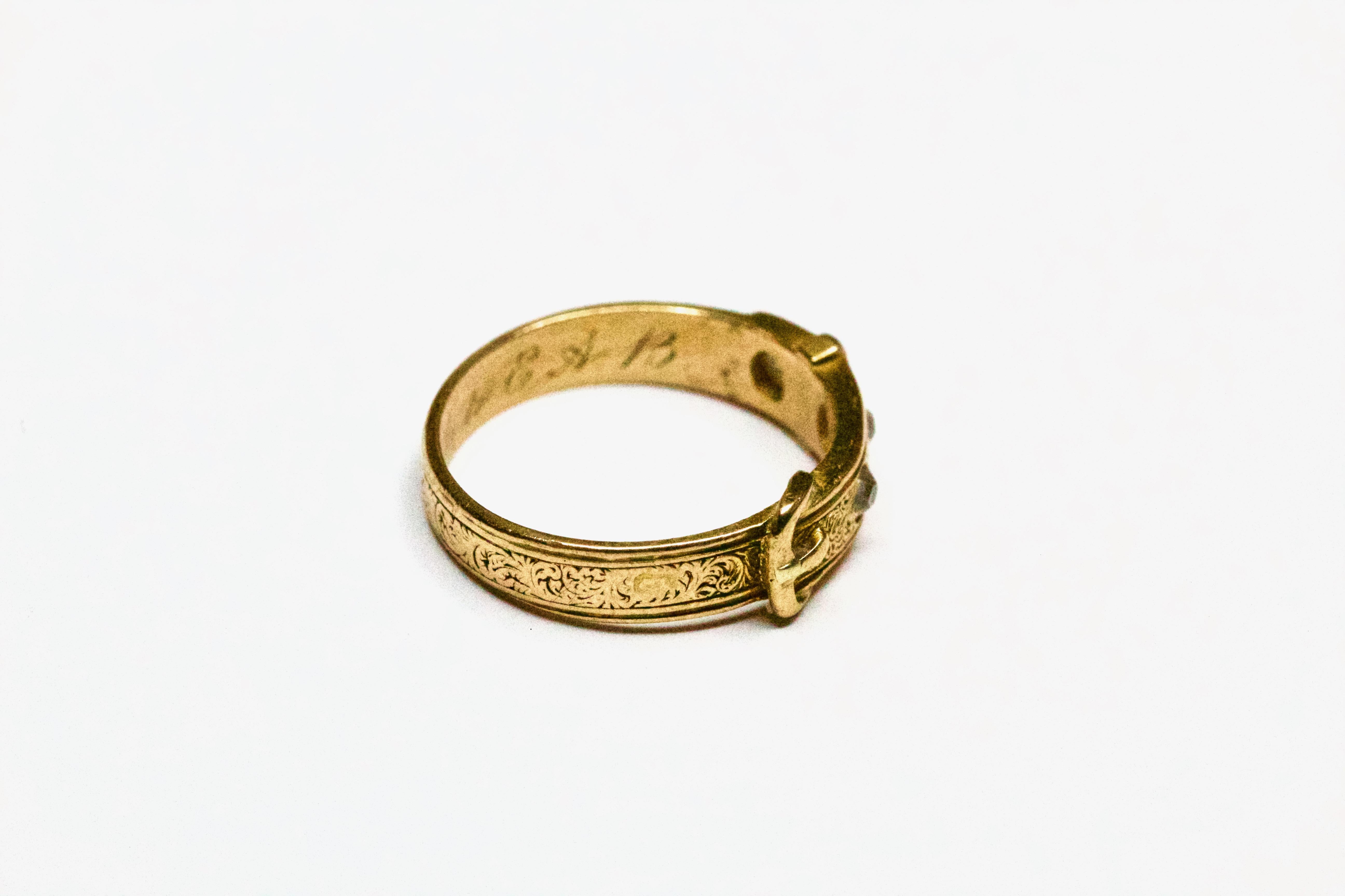 This stunning ring, made of solid 18 carat yellow gold, is hallmarked inside the shank for London 1860. The buckle design is embellished with three old mine cut diamonds and delightfully hang engraved throughout. it has an inscription inside reading