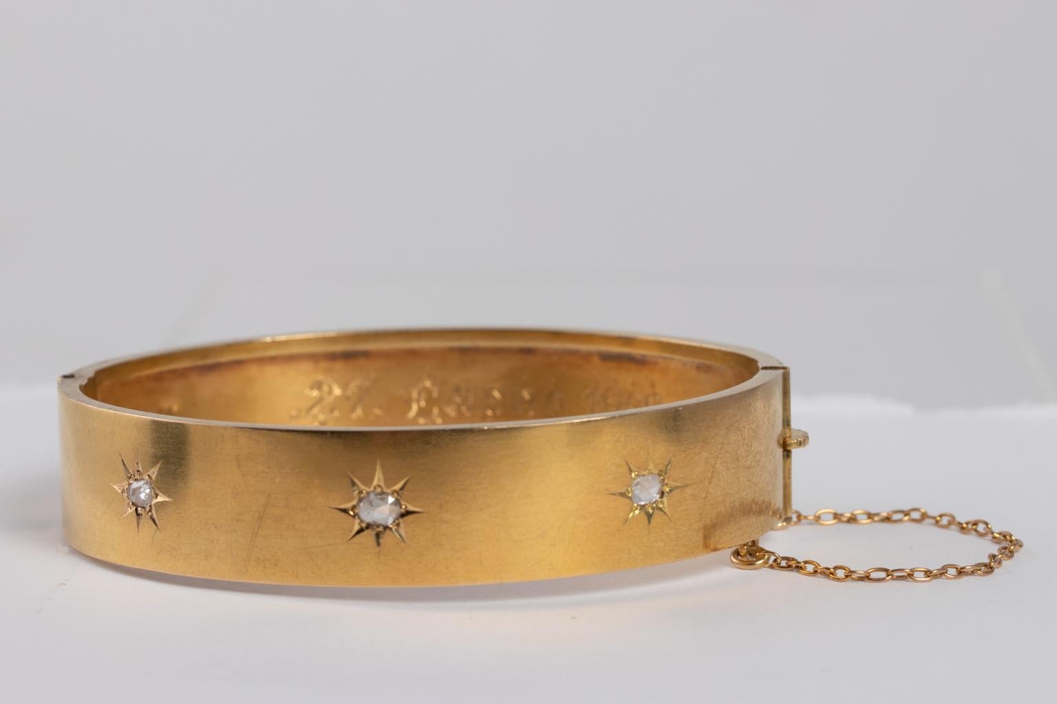 Circa 1900s late Victorian 18 karat bangle bracelet set with three rose cut diamonds in a star motif. It is hand inscribed with name and dated 1902 on the inside. The patina of the bracelet is a rich gold and features a safety chain built into the