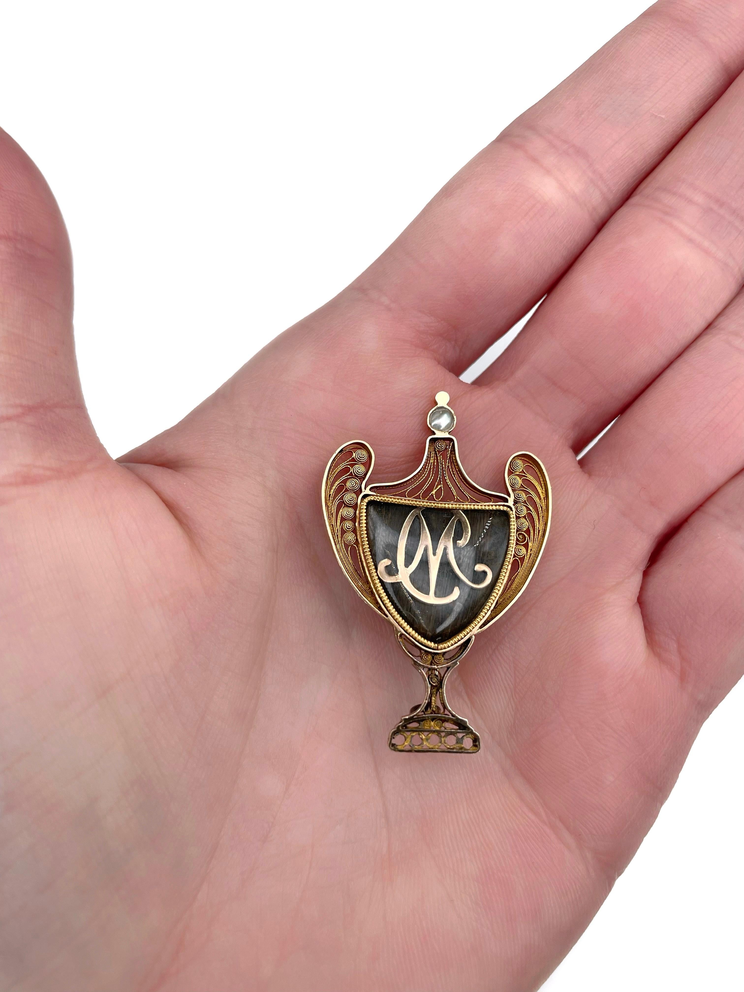 This is a Victorian mourning brooch with initials in a shape of the urn vase. It is crafted in 18K gold using a filigree technique. Circa 1880.

The piece features a hairwork (covered with the glass). The top is encrusted with a pearl.

This is an