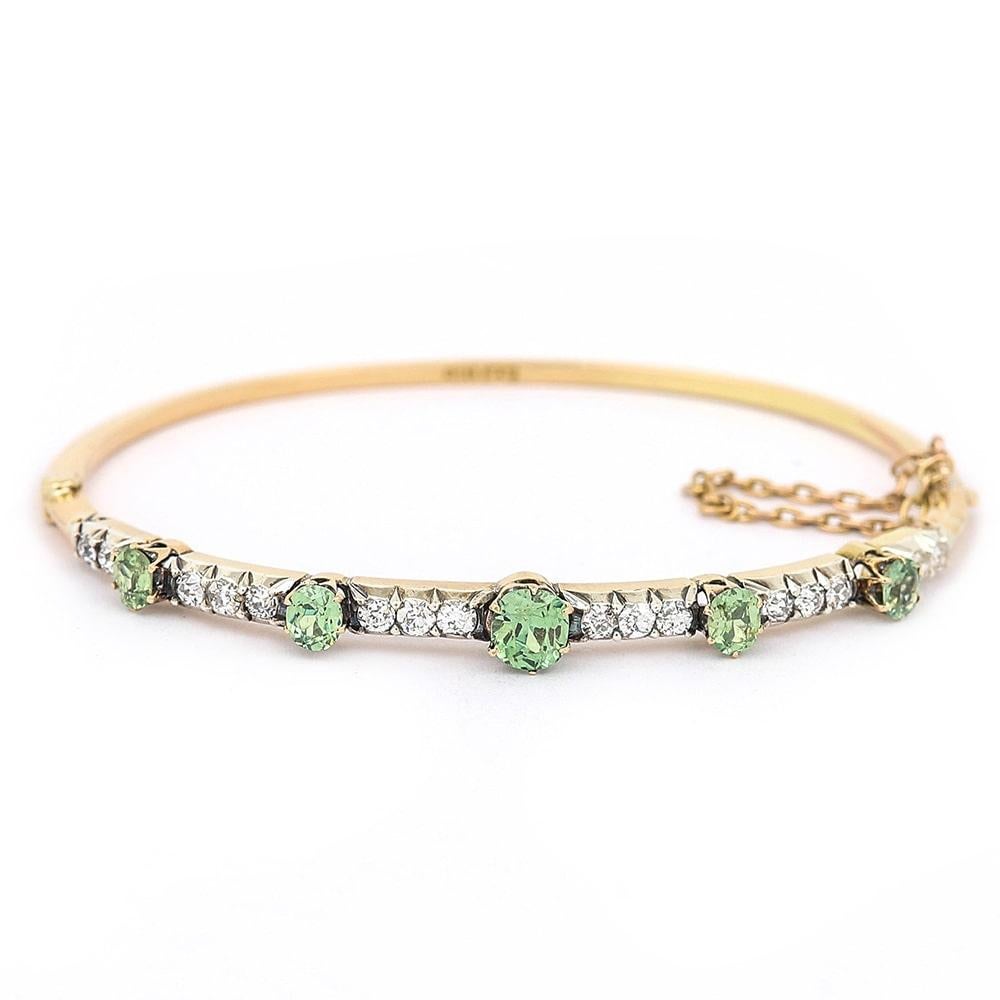 An attractive 18 karat yellow gold Victorian peridot and diamond bangle, comprising five peridots with an estimated 0.50 carats of peridots. Also an estimated 1.05 carats of Old European cut diamonds, claw set in silver. This antique hinged bangle