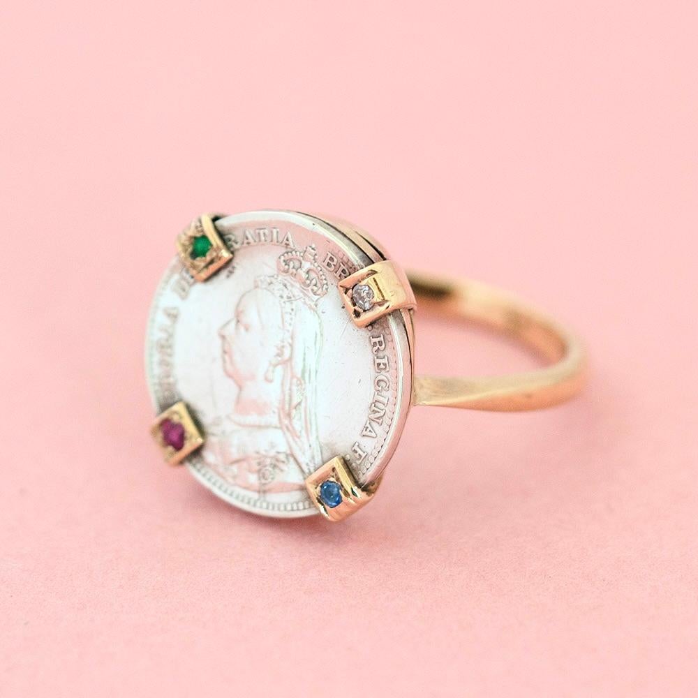 This fascinating ring unites two eras of craftsmanship — an antique Victorian silver coin from 1890, artfully set into a later 9ct gold band. The coin, depicting Queen Victoria, has been mounted in four gold prongs, each adorned with a gemstone:
