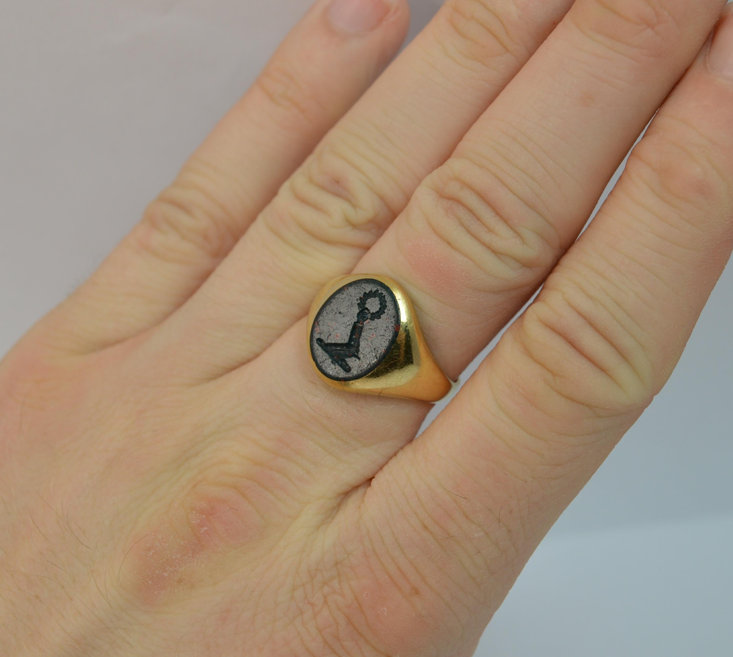 A stunning 18 carat gold and bloodstone signet ring.
SIZE ; P UK, 7 3/4 US
Solid 18 carat gold with single bloodstone to centre.

Set with a single oval bloodstone panel with intaglio of an arm in armour reaching up holding a wreath.

10mm x 13mm