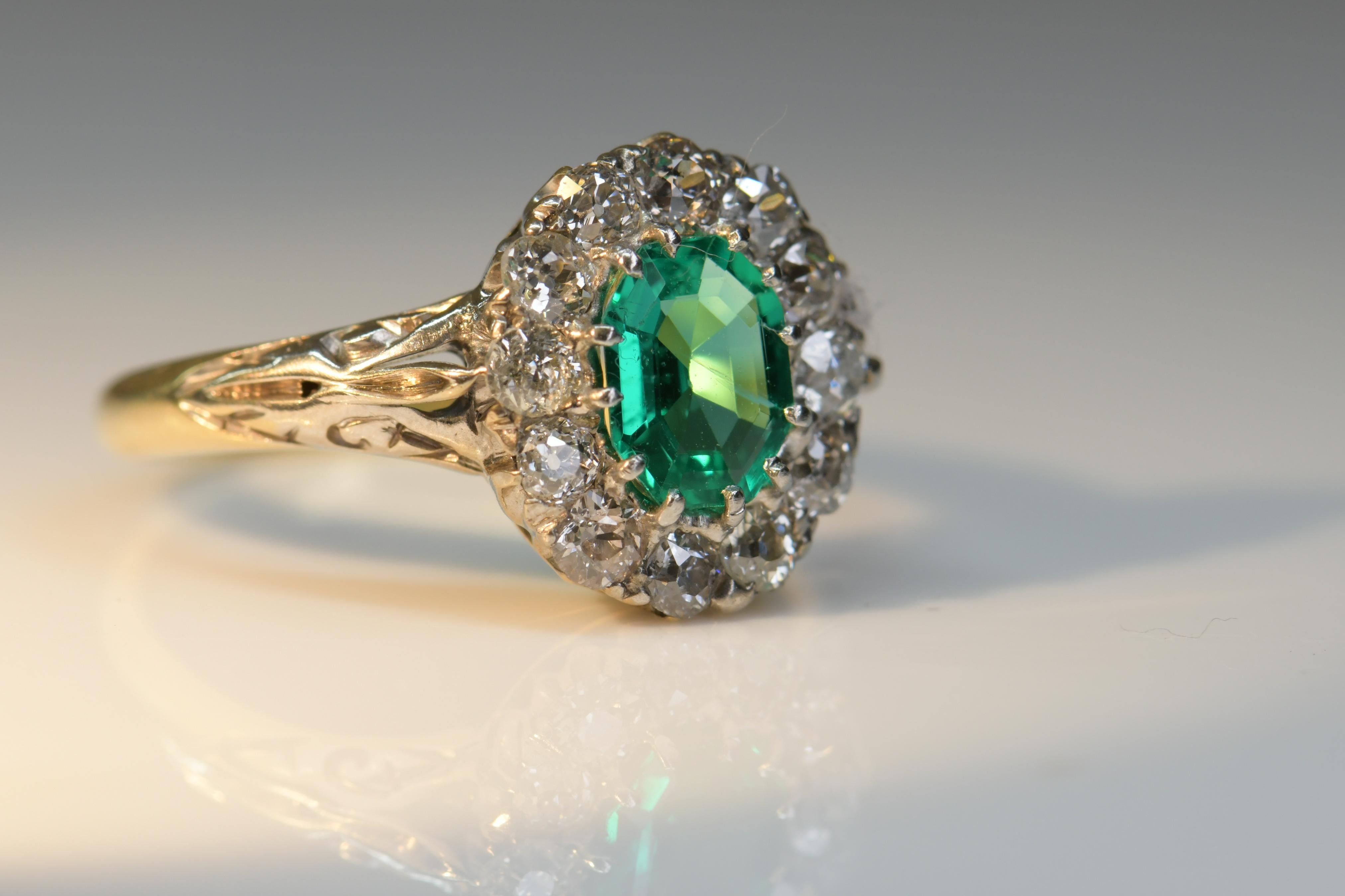 An impressive Victorian emerald and diamond cluster ring made in 1880 with very elegant scrolling decoration to the shoulders. The emerald is a top gem quality Columbian emerald, the stone is super clean which is very rare in emeralds, accompanied