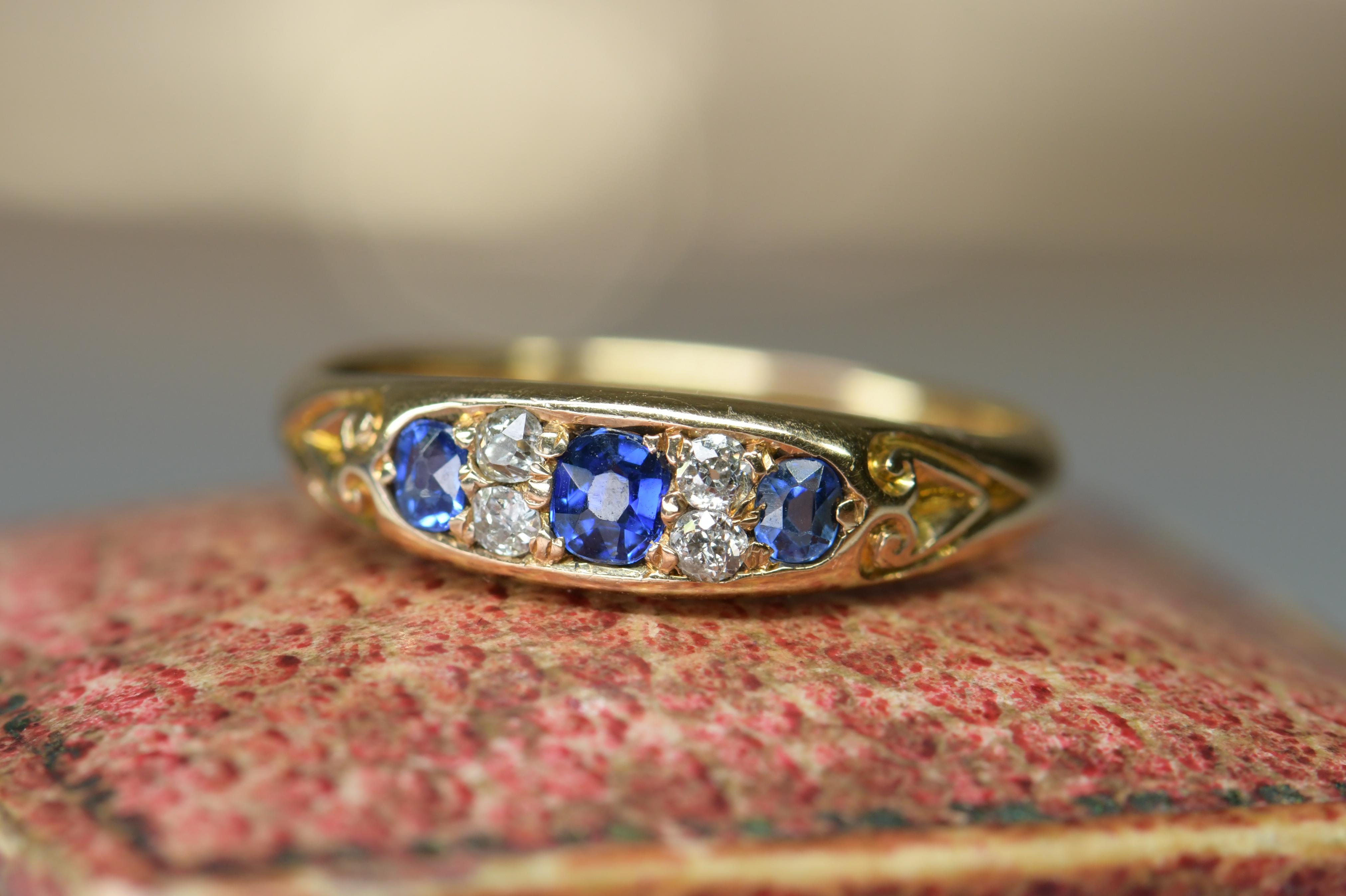 A good looking Victorian 18ct gold ring. It is set with three oval sapphires with small diamonds in between. The shoulders have unusual incised decoration and are very much part of the overall design. It would be ideal as an engagement ring. The