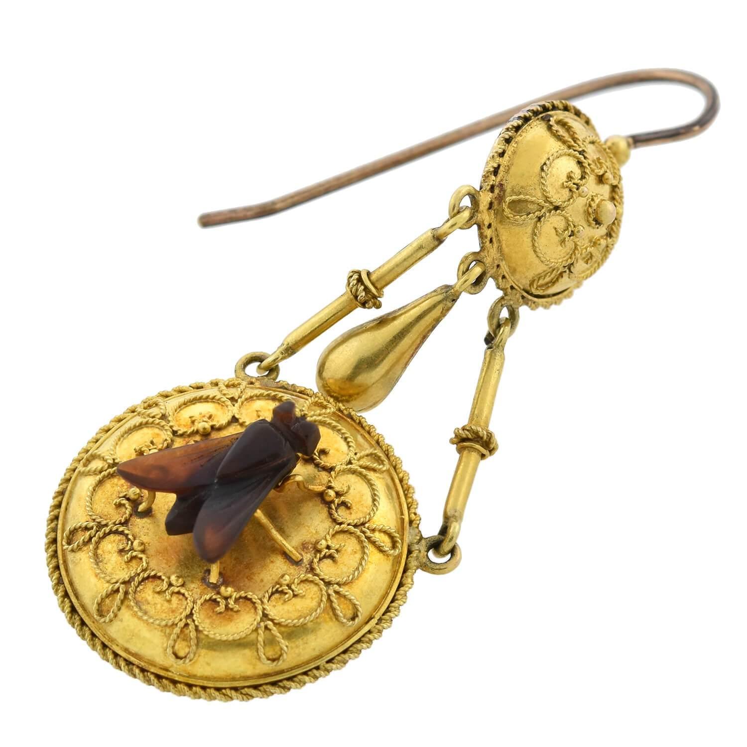 An unusual and exquisite pair of earrings from the Victorian (ca1880s) era! Crafted in blooming 18kt yellow gold, these superb earrings begin with a simple earring wire above a round topper. The surmount is slightly convex and ornately adorned with