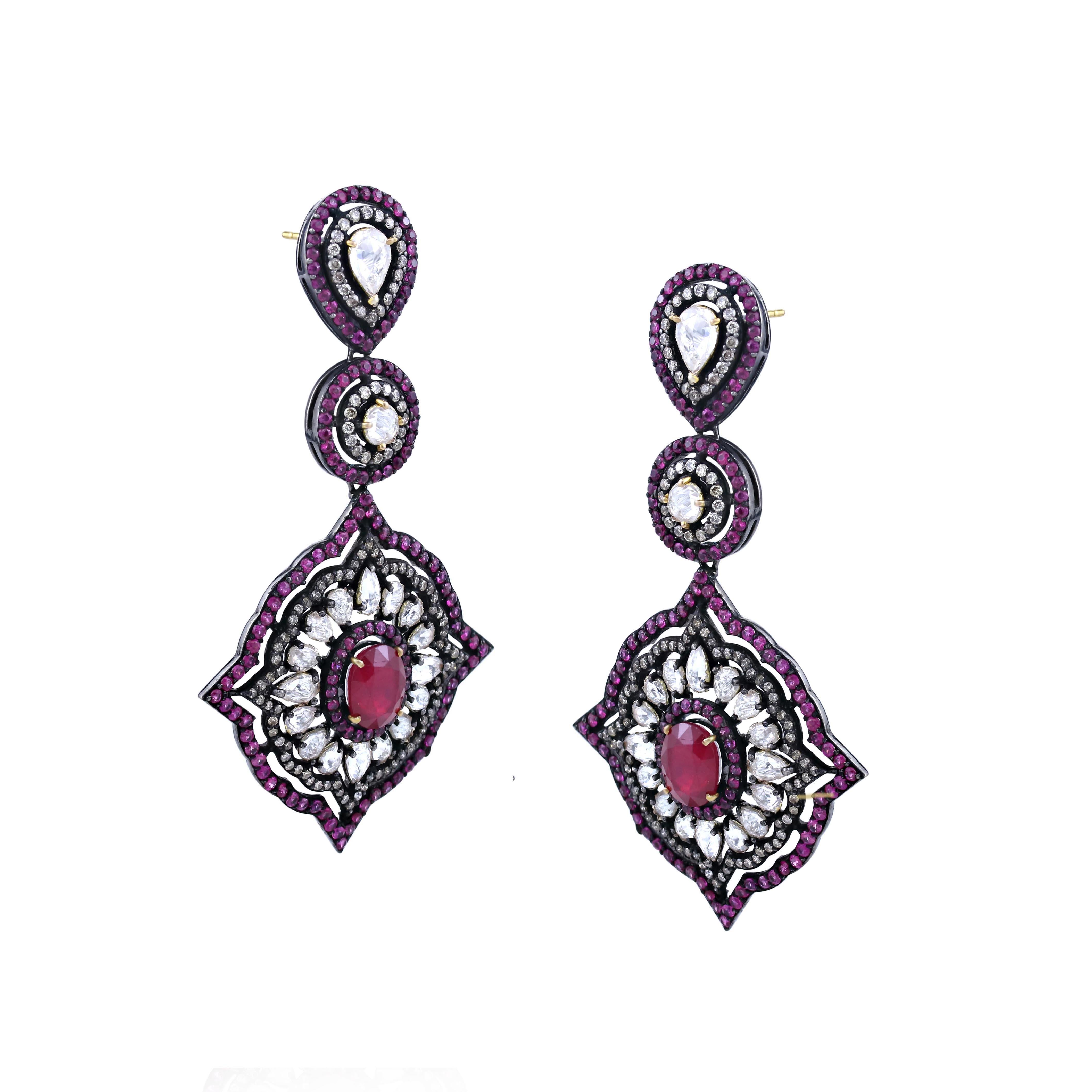 Presenting a mesmerizing display of color! These drop earrings boast of pear, round and floral motifs. The pear and round motifs hold white sapphire at center enclosed in diamond ruby halos. The large floral motif at the bottom has oval ruby at the