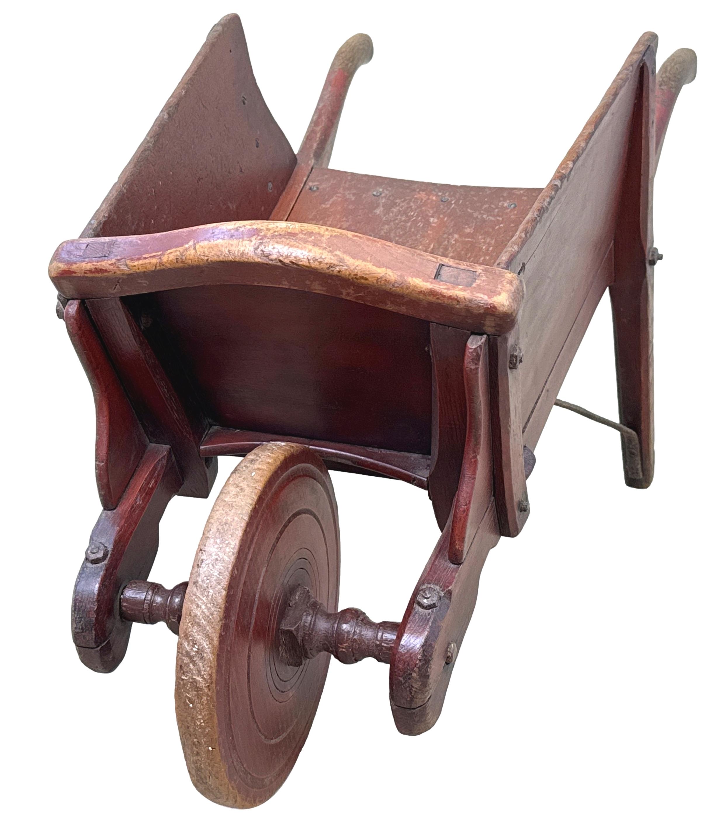 Brouette pour enfants en orme de la période victorienne du milieu du 19e siècle, extrêmement intacte et originale. Elle a conservé son attrayante finition en peinture rouge d'époque, ses élégantes poignées en forme d'origine, ses côtés solides et sa