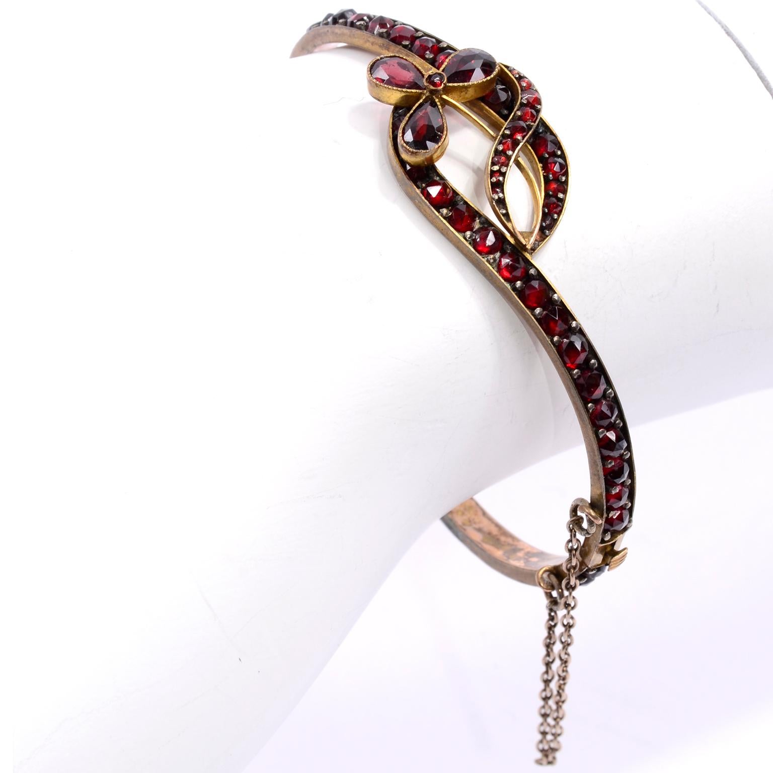 This is a pretty antique 19th Century Victorian bohemian garnet bracelet in a bangle style with a push clasp and chain. The design creates a little loop and a flower.  There is some wear/discoloration to the gold finish on the inside of the bangle