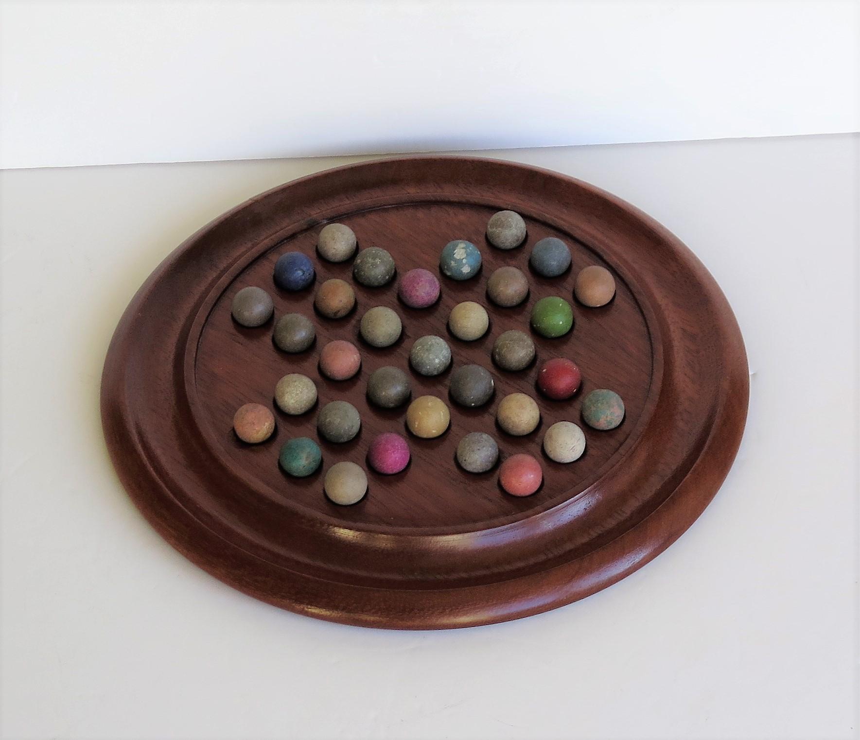 This is a complete marble solitaire game, having a very good hardwood board and a complete set of 33 clay or stone handmade marbles, all dating to the 19th century Victorian period, circa 1860.

This board is circular hand-turned and made of a