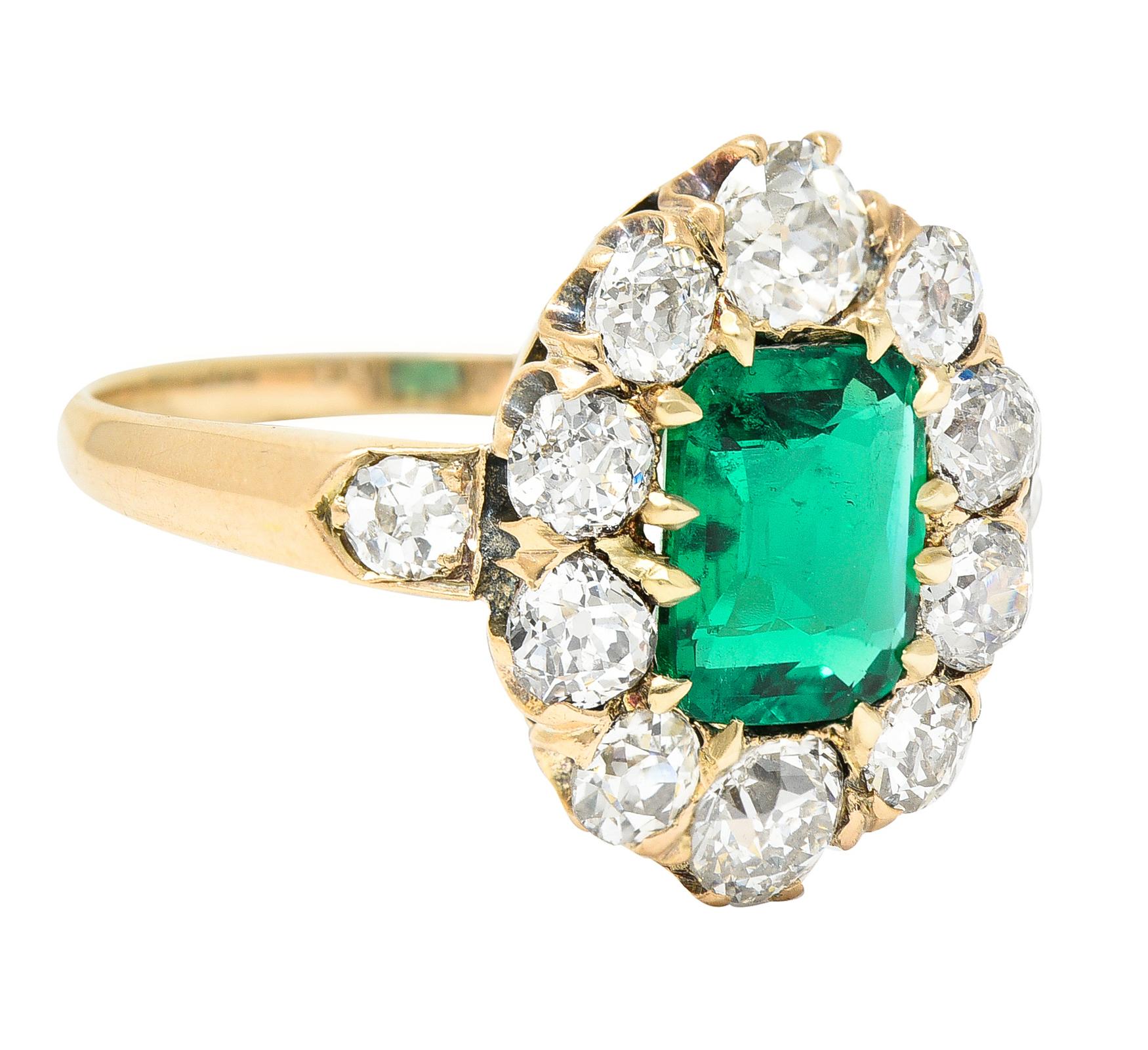 Centering a mixed cushion cut emerald weighing 1.05 carats total - prong set. Colombian in origin with minor traditional clarity enhancement. Transparent bright green in color - prong set with cluster surround. Featuring old European cut diamonds -