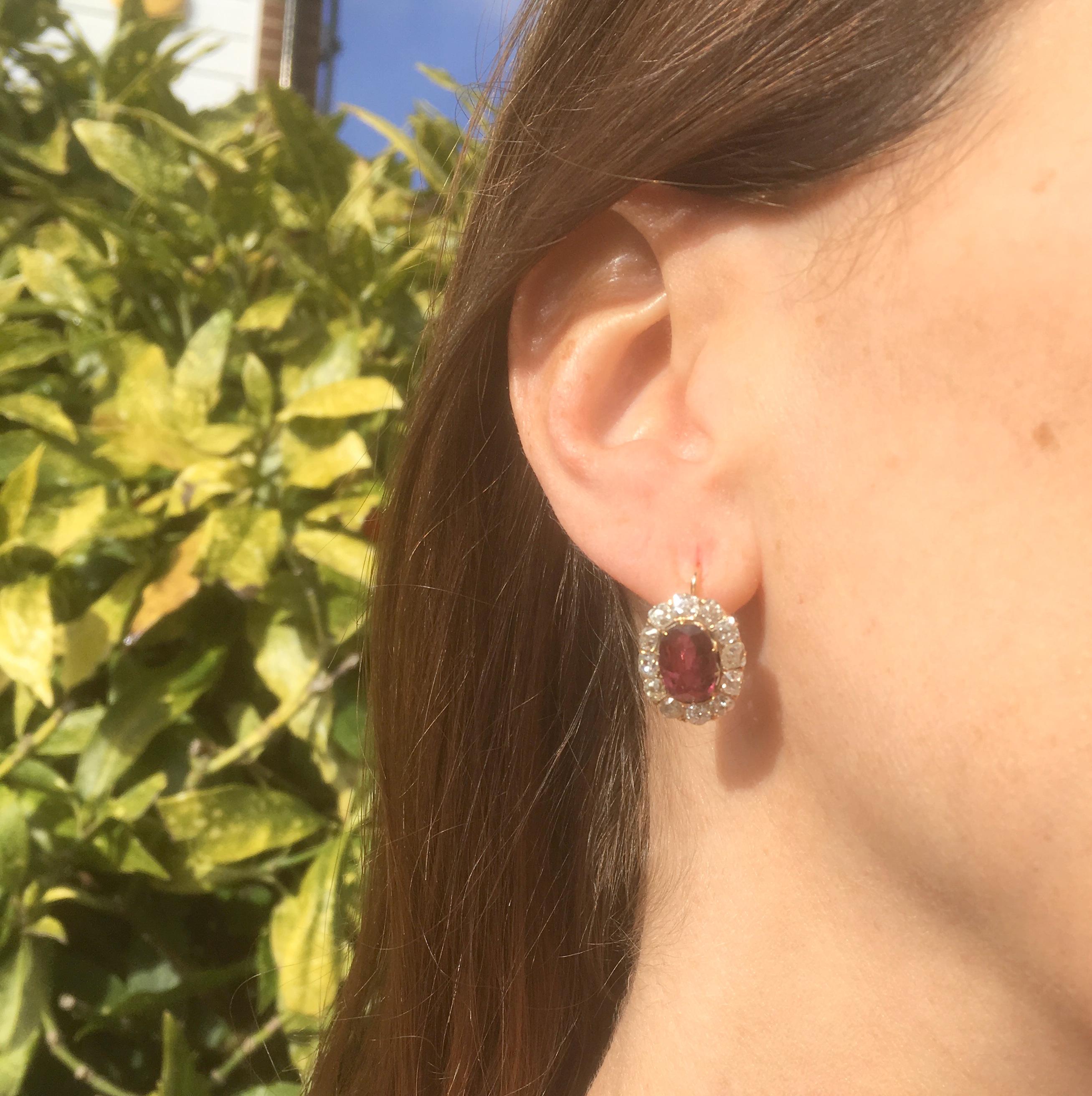 A striking pair of ruby and diamond cluster earrings. Each of the rubies displays a strong pinkish red, the tone of which is emphasised by the border of twelve white and bright old cut diamonds in the surround. The finely pierced coronet gallery