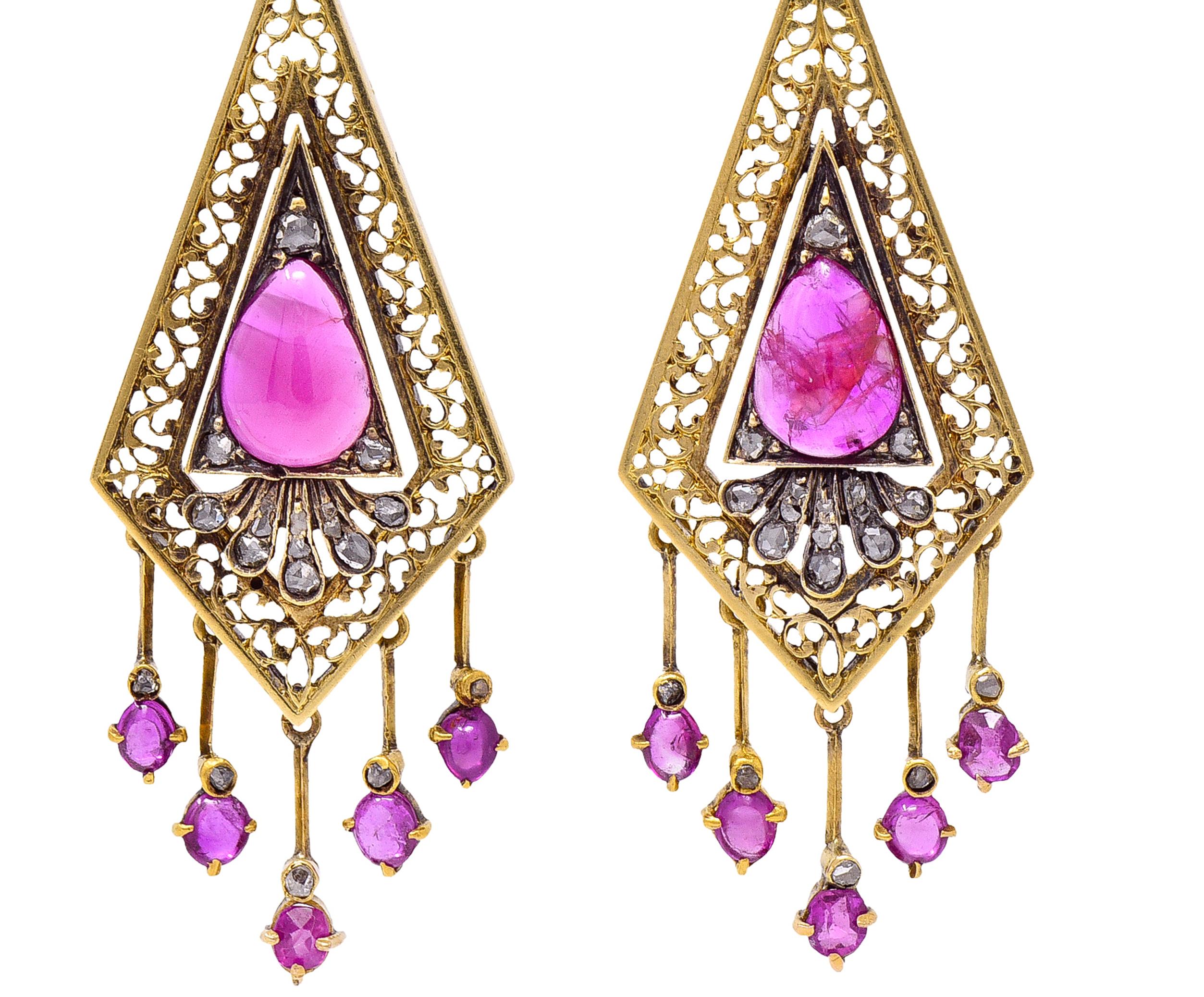 Comprised of bow motif surmounts suspending kite shaped drops with an articulating fringe. Featuring pear shaped ruby cabochons bead set in triangular frame surround. Centered on pierced scroll motif kite drop - semi-transparent purplish pink in
