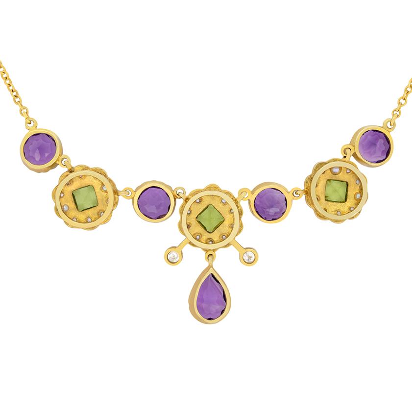 This Victorian necklace exudes elegance with a series of rub over set amethysts, including a central pear cut and four round cuts totalling 5.50 carat. Sitting in between the amethysts, are three beautiful daisy clusters with square cut peridots and