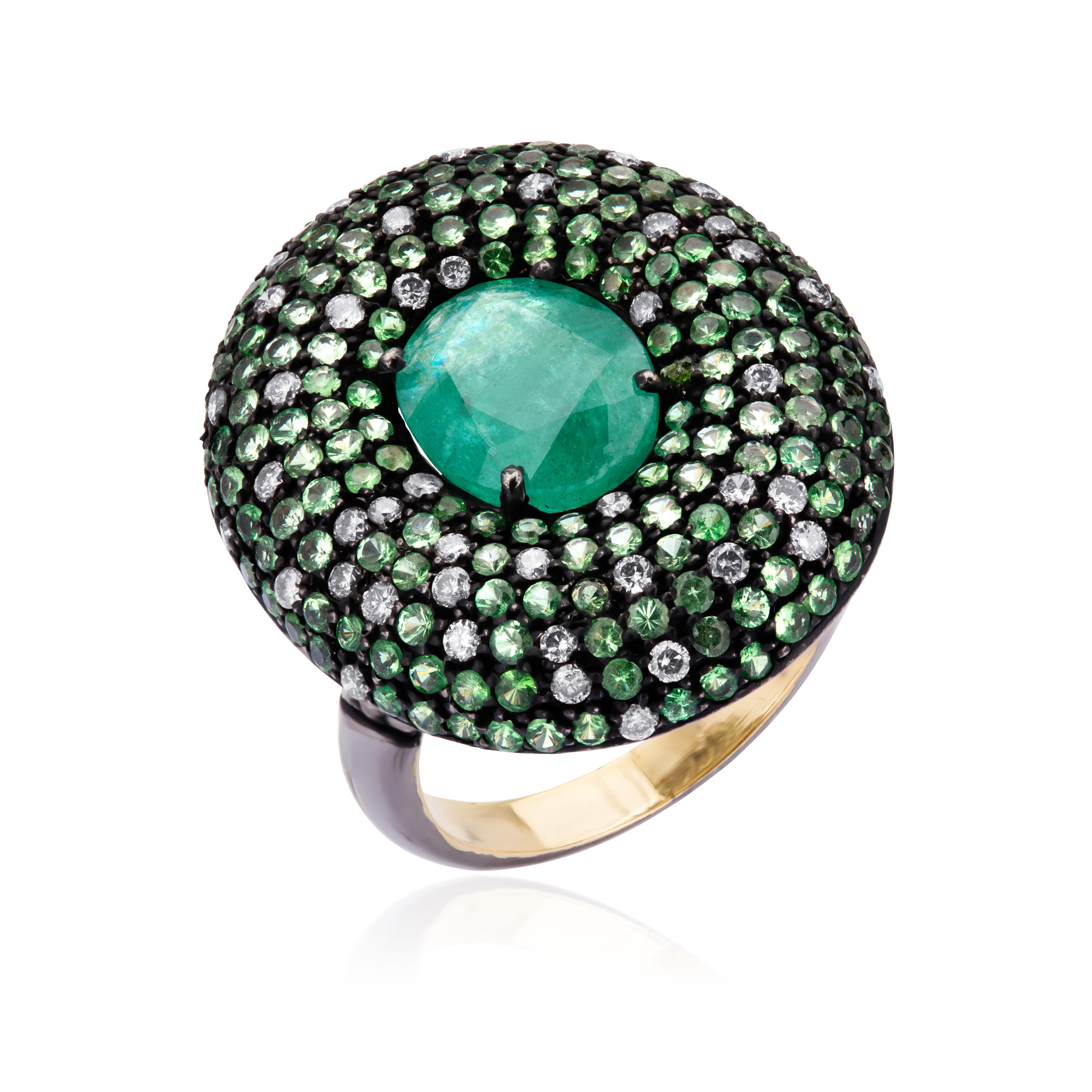 Hand fabricated in rhodium over 18K gold, this exquisite finger bauble, is crowned with an oval faceted emerald 2.67 Cts glittering within a curve circular frame embellished with diamonds (IJ Color, SI Clarity) and Tsavorite, all supported by
