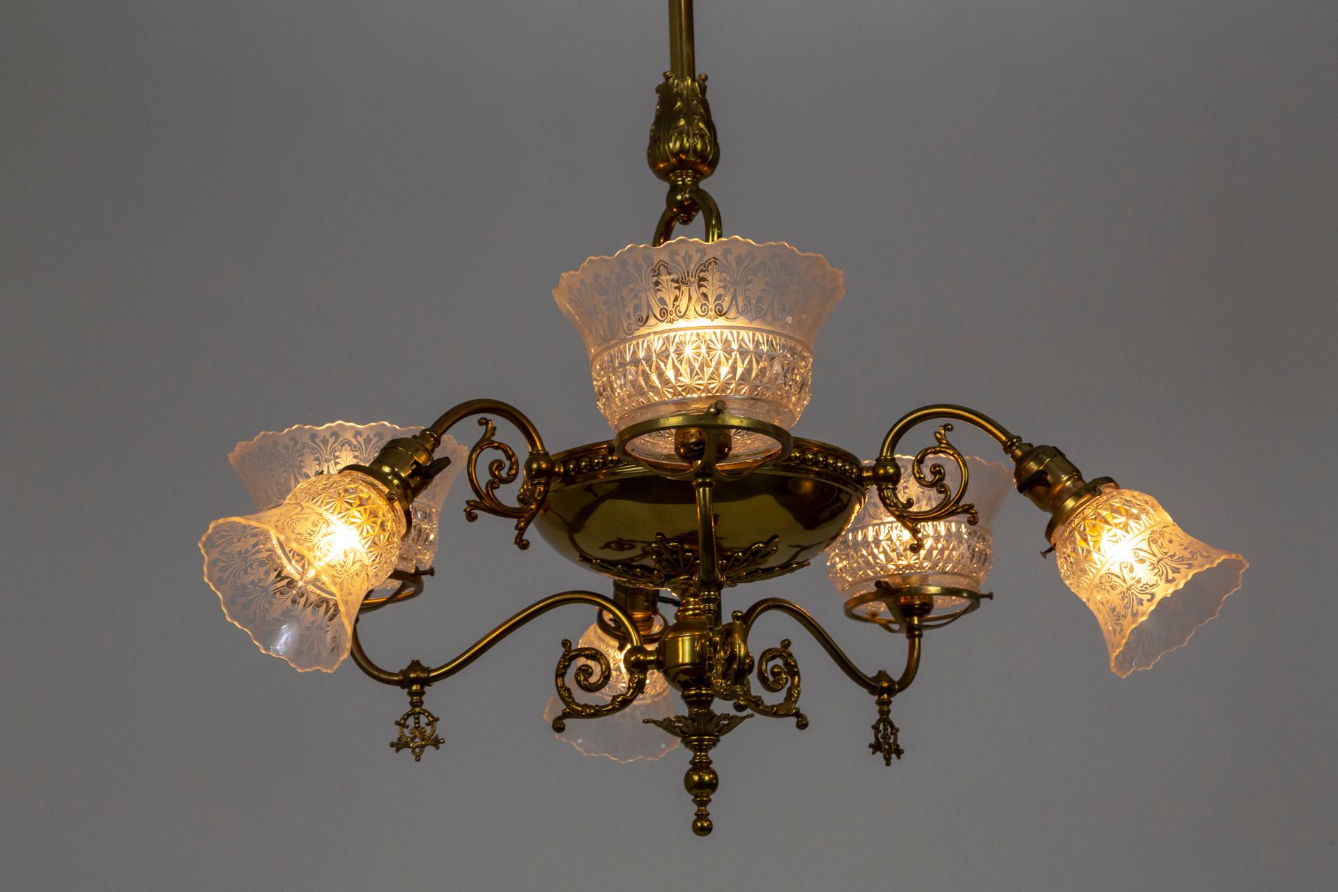 A Victorian, brass chandelier alternating between larger up lights and smaller down lights. The original shades are molded, etched glass in bell form with scalloped edges. A lengthy, substantial stem and acanthus leaf accents, scroll arms and large,
