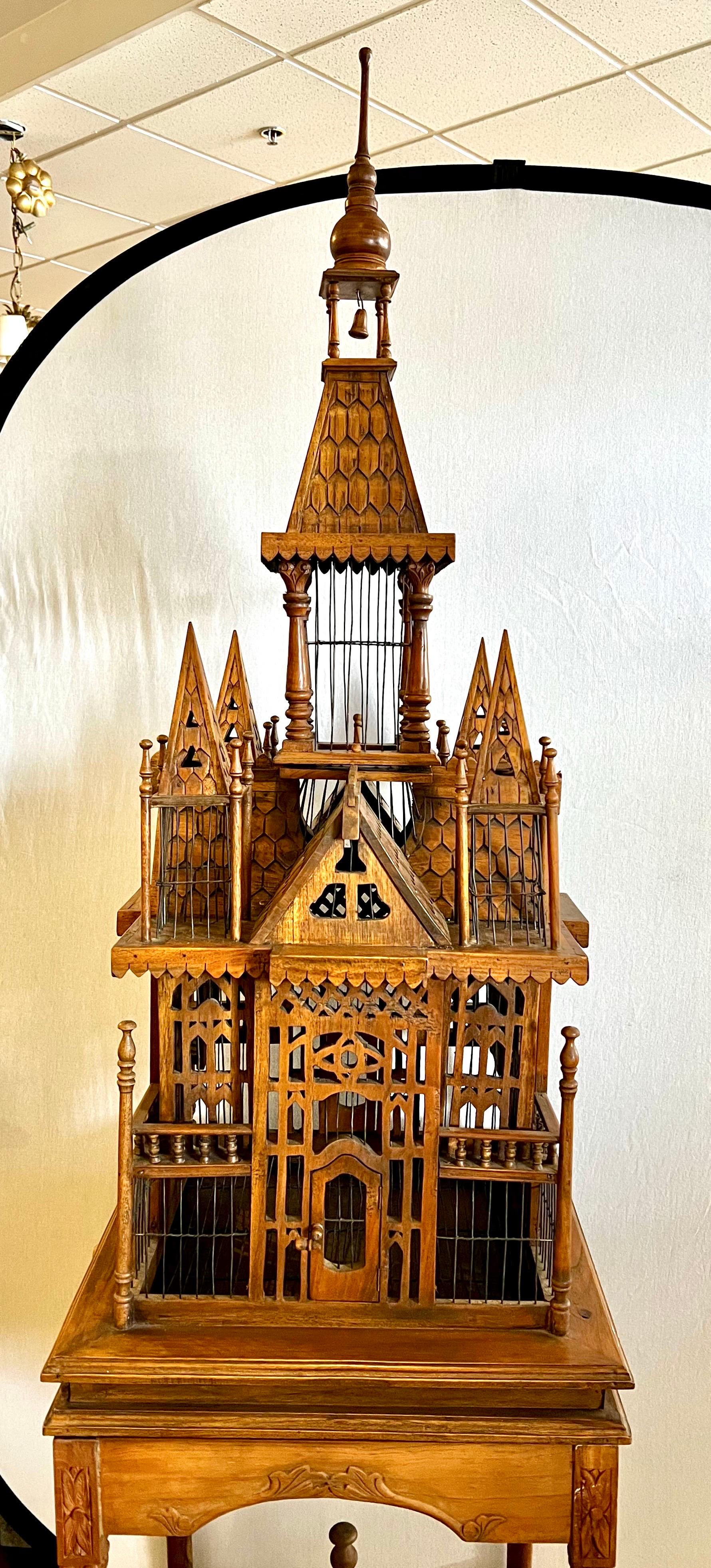 Exquisite bird cage on stand featuring intricately hand carved mahogany Victorian style palatial structure with a porticoed temple and spires on the tops. Mounted on a carved square table with elegant tapered legs and a carved apron and slide out