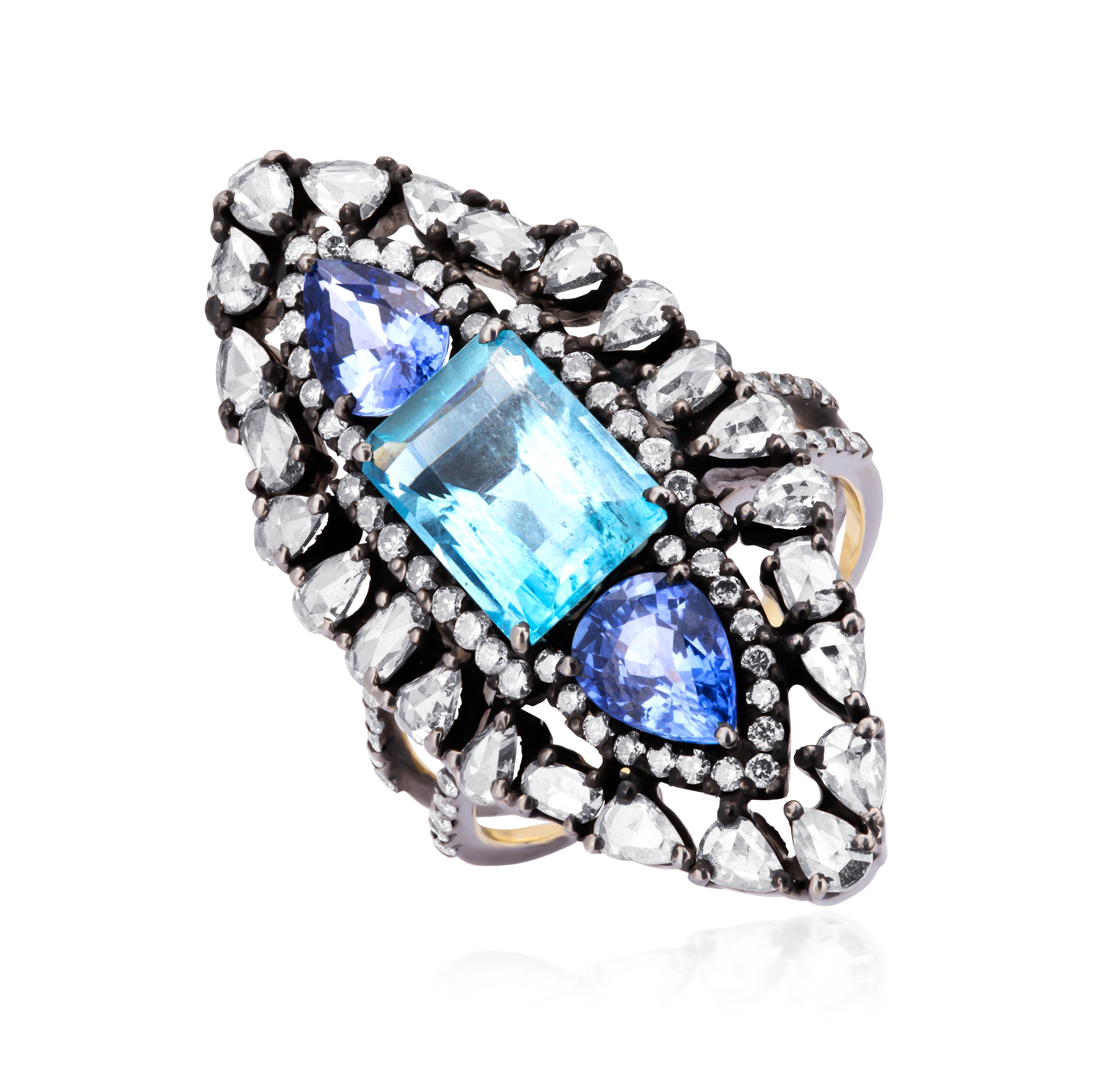 A gorgeous emerald cut aquamarine, weighing 2.6 Cts enhanced with two blue sapphires on each side sits in a sparkling marquise shaped frame of diamonds. The center design is stabilized with a split shank band adorned with more diamonds. Crafted in