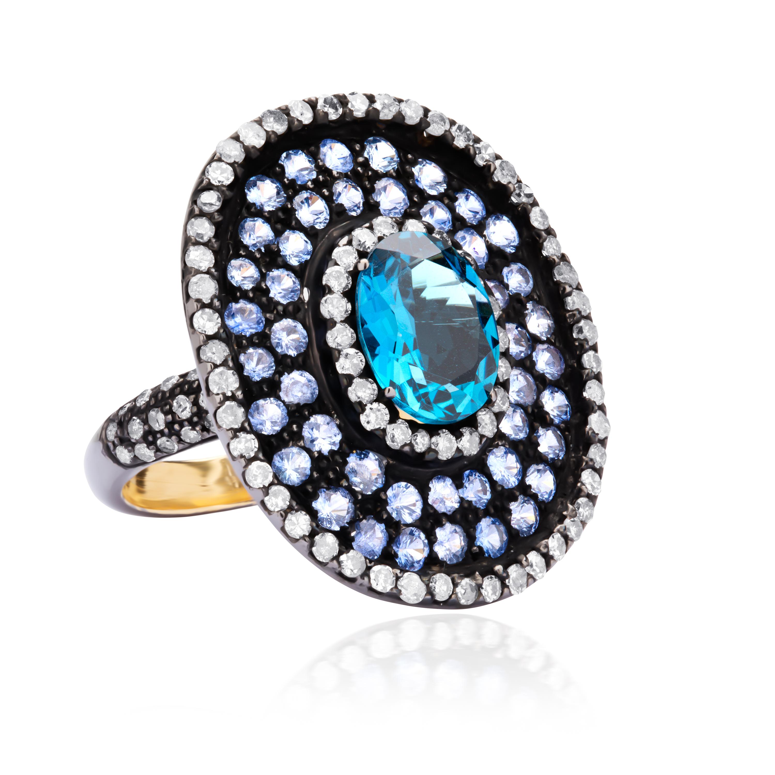Crafted over 18K gold and sterling silver, this exquisite finger bauble, is crowned with an oval faceted blue topaz 2.58Cts glittering within a circular frame embellished with blue sapphires and diamonds  (IJ Color, SI Clarity), all supported by