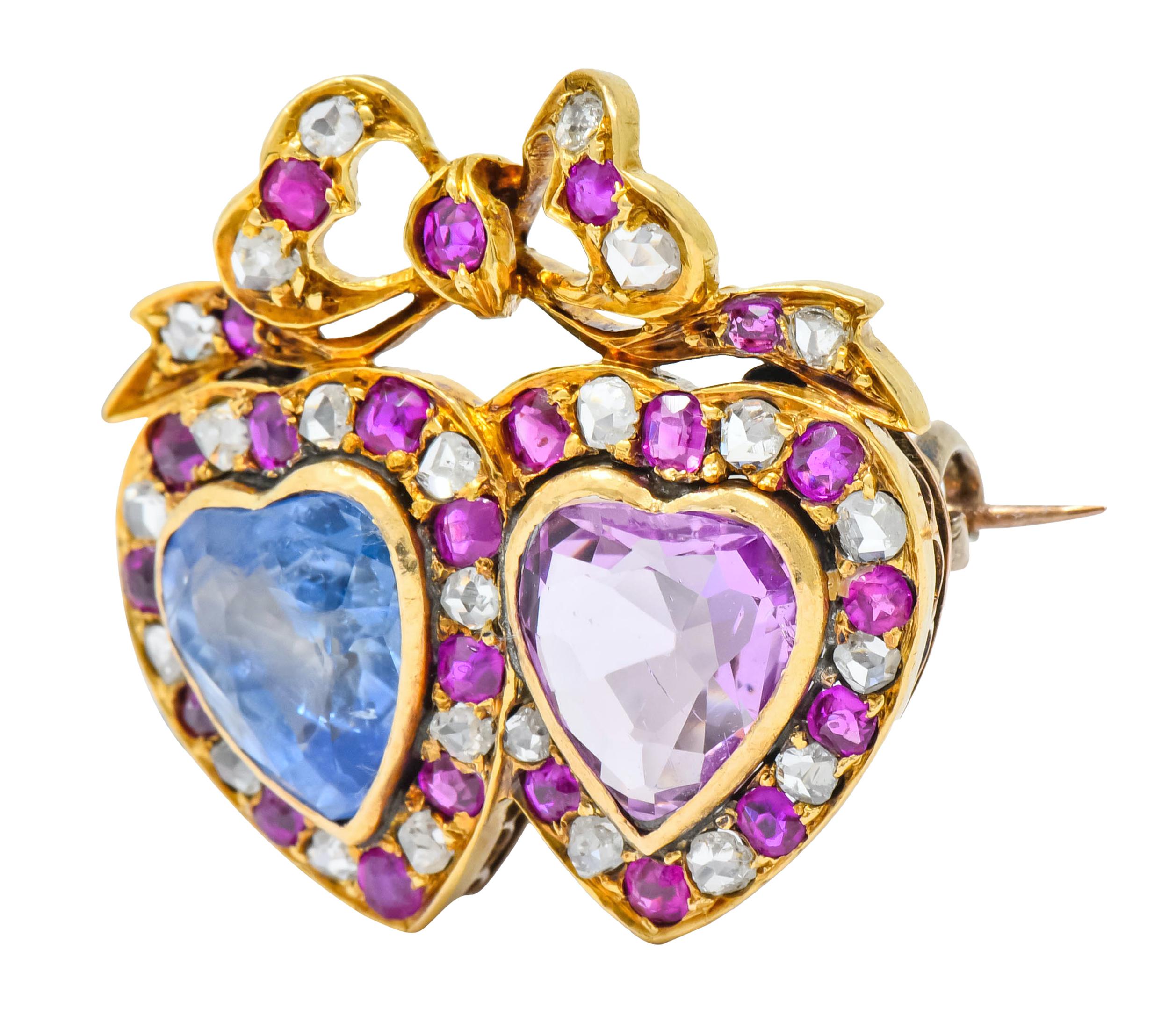 Brooch designed as two hearts topped with a bow motif

Each heart centering bezel set heart cut sapphire

One a powdery light blue, the second, a very-light bubble gum pink weighing approximately 6.50 carats total

Surrounded by round cut rubies