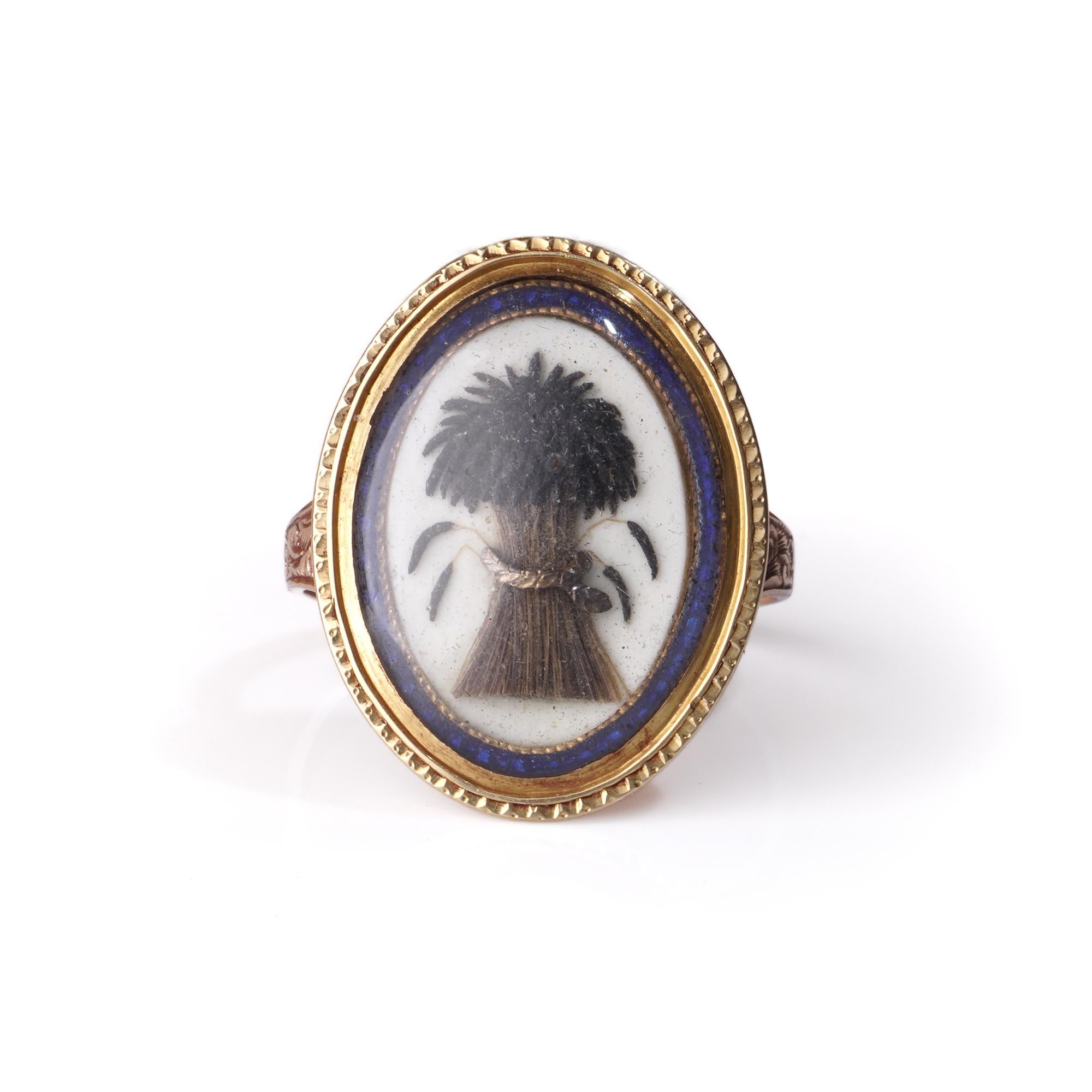 This Victorian mourning ring is crafted in 9kt gold and features an intricately preserved hairwork design under a protective crystal panel. The central motif depicts a sheaf of wheat, symbolising the harvest of life and eternal rest — a popular