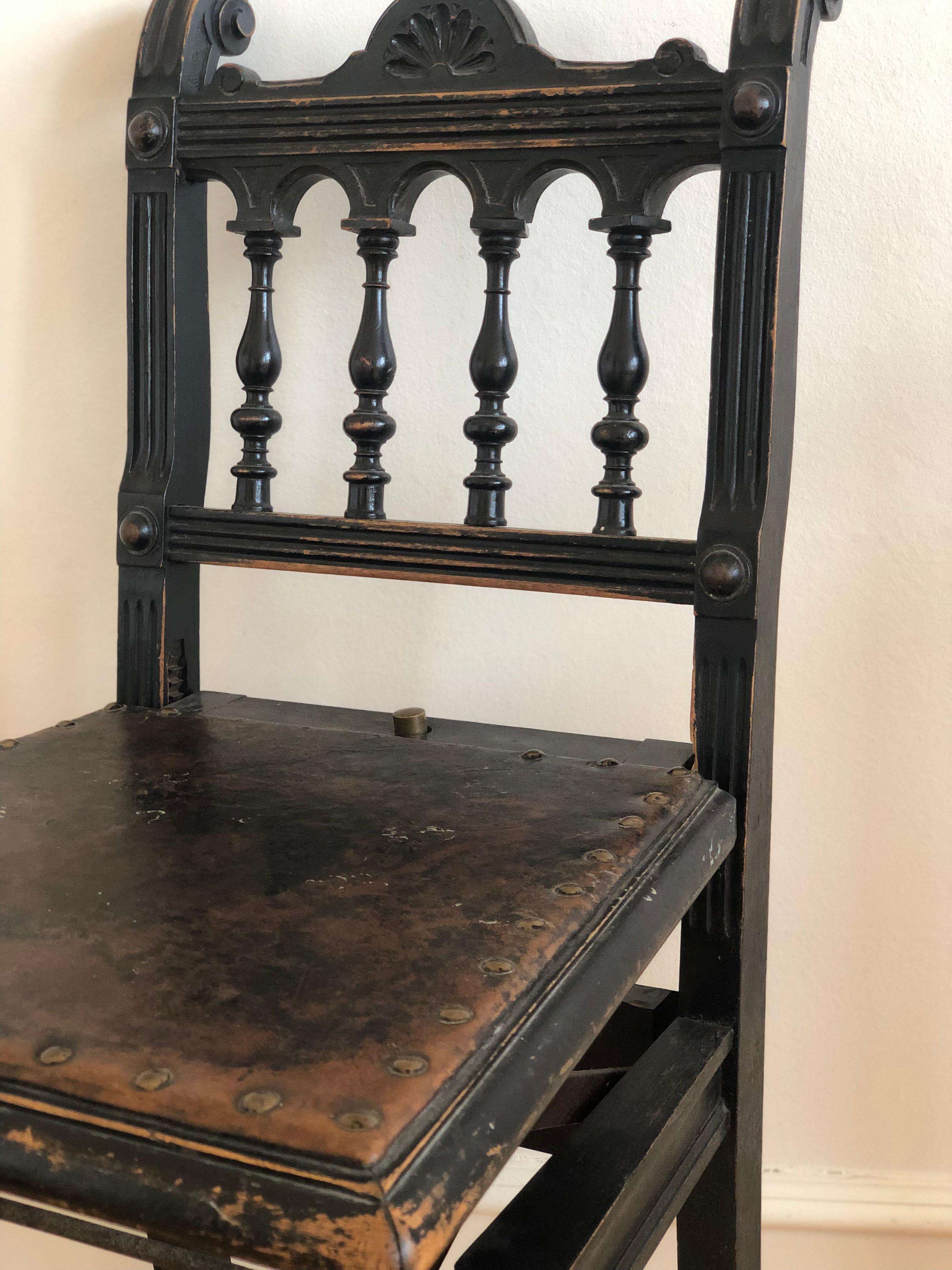 Victorian black-painted concert chair with adjustable leather seat on a hinged mechanism. Crafted around 1900, the chair features turned spindles, decorative crest, and an authentic aged patina. The seat height is adjustable via a mechanical lift