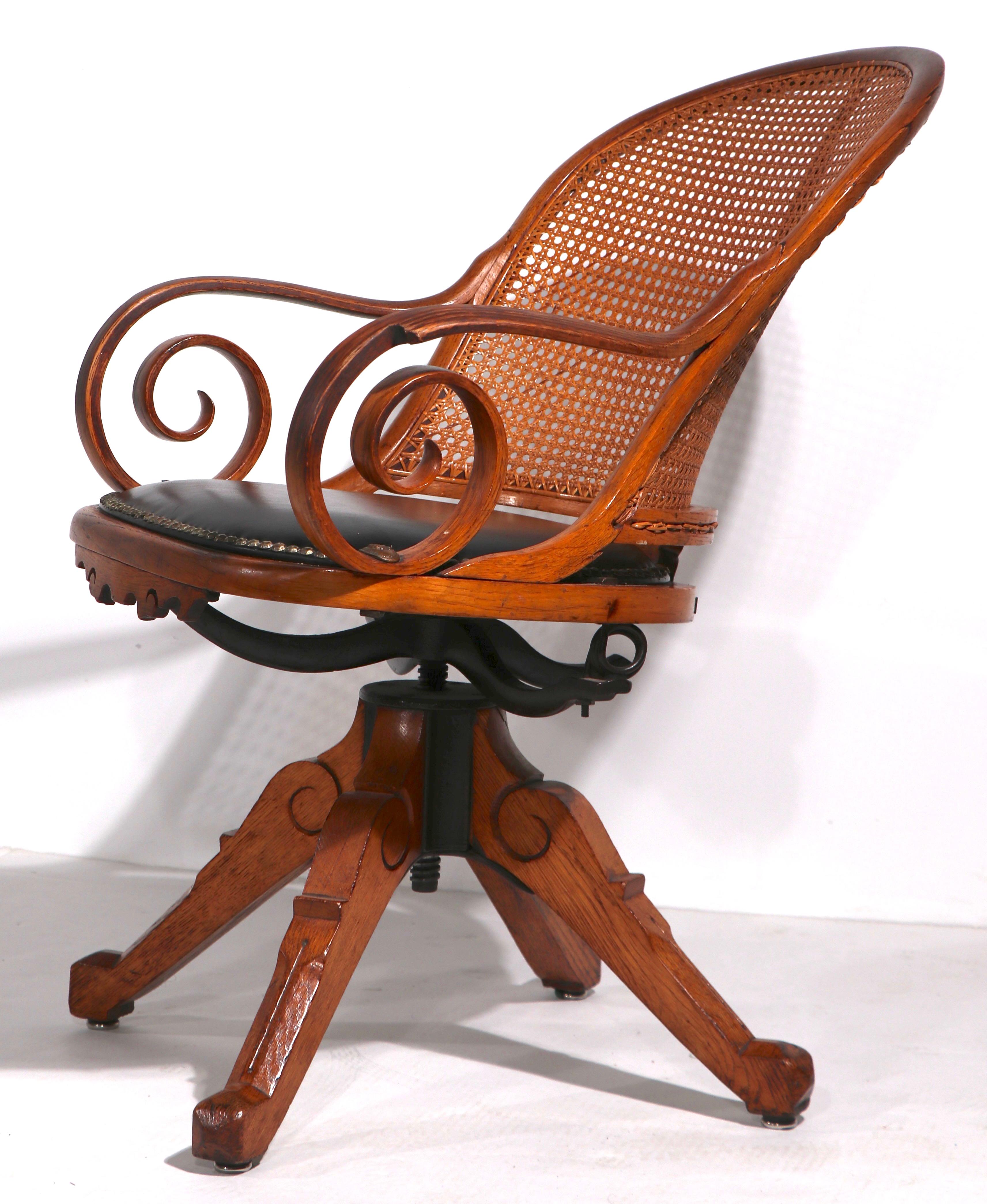 Top quality Victorian swivel desk chair with caned back, and metal medallion joinery. The chair features bentwood curlicue arms, and a four leg pyramid form base. Design attributed to Charles Eastlake, Aesthetic Movement period production. This