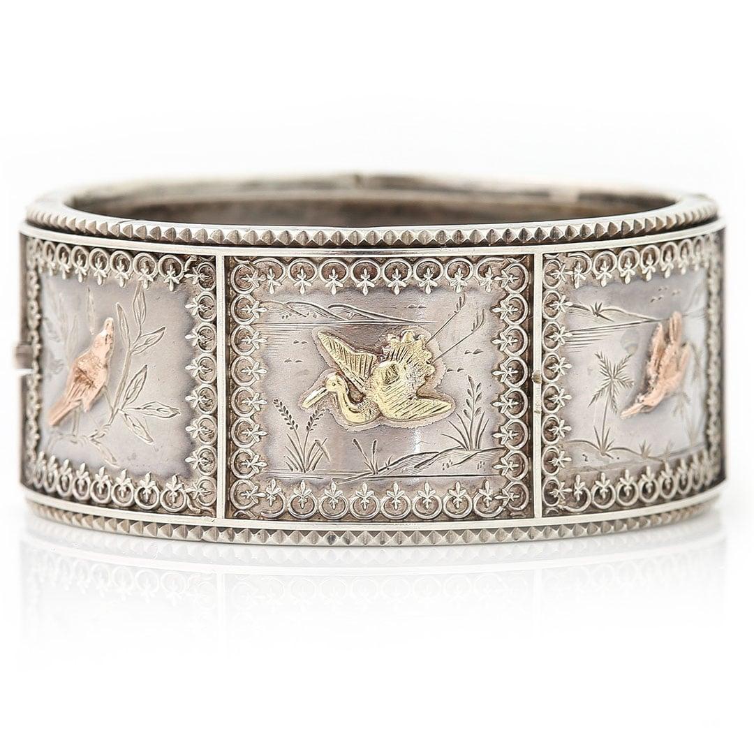 This beautiful Victorian silver cuff bangle was created during the height of the Aesthetic movement during the 1870-80s when silver jewellery was most popular amongst the elites. This bangle has applied yellow and rose gold bird motifs and was
