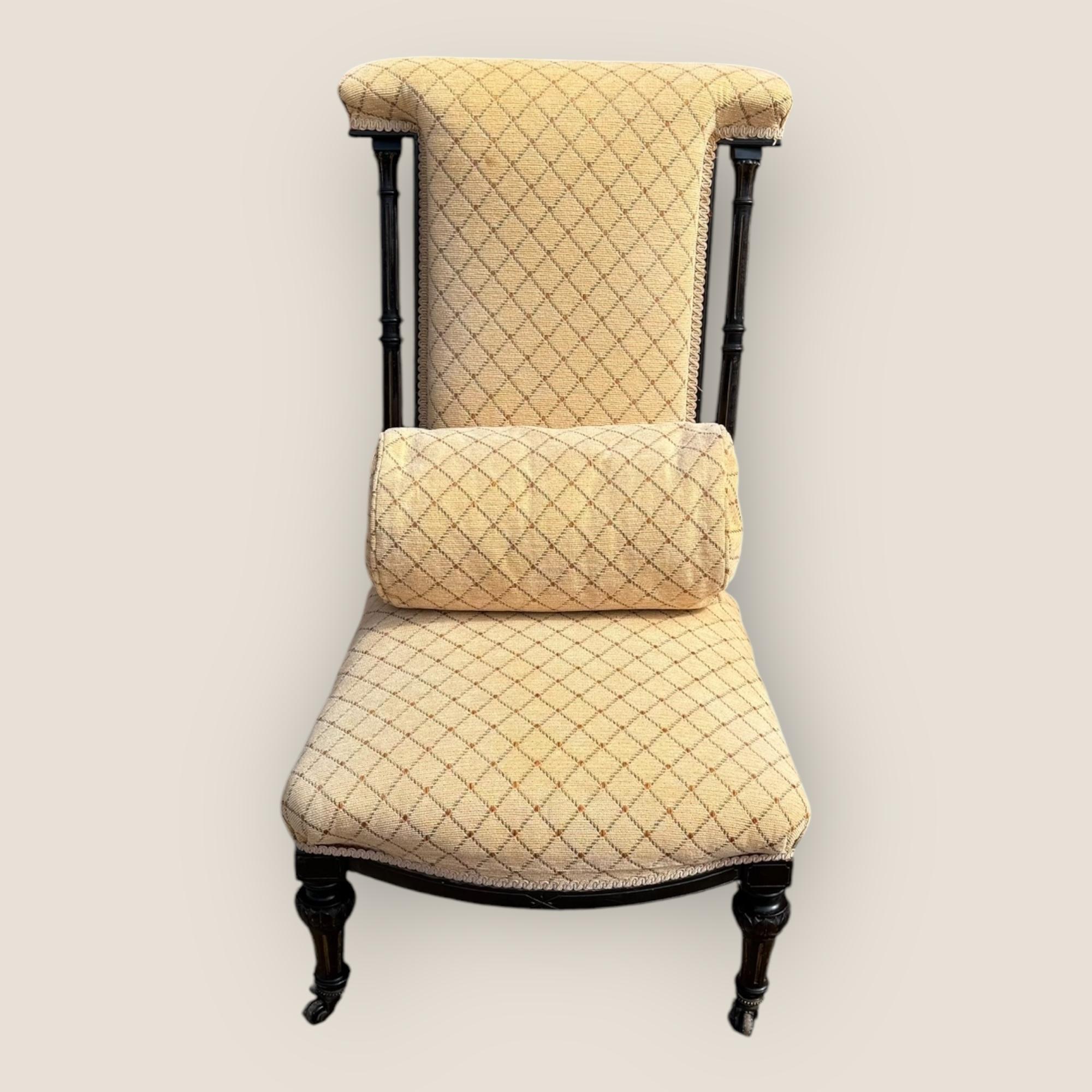 Nous avons ici une chaise de prière de style esthétique victorien (1837-1901) avec un coussin. Cette chaise de prière a un cadre en bois ébonisé, le dossier de la chaise a des colonnes corinthiennes de chaque côté et des roulettes sur les pieds. La