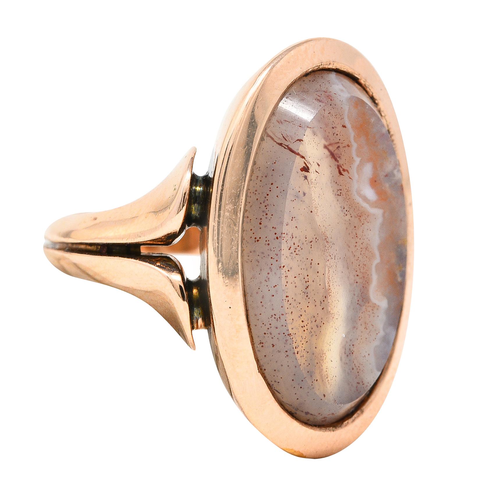 Ring centers a beveled oval shaped agate tablet measuring 11.5 x 18.5 mm. Translucent peach with white and red swirling - bezel set in rose gold frame surround. With split fluted shoulders and grooved shank. Competed by high polished finish. Tested