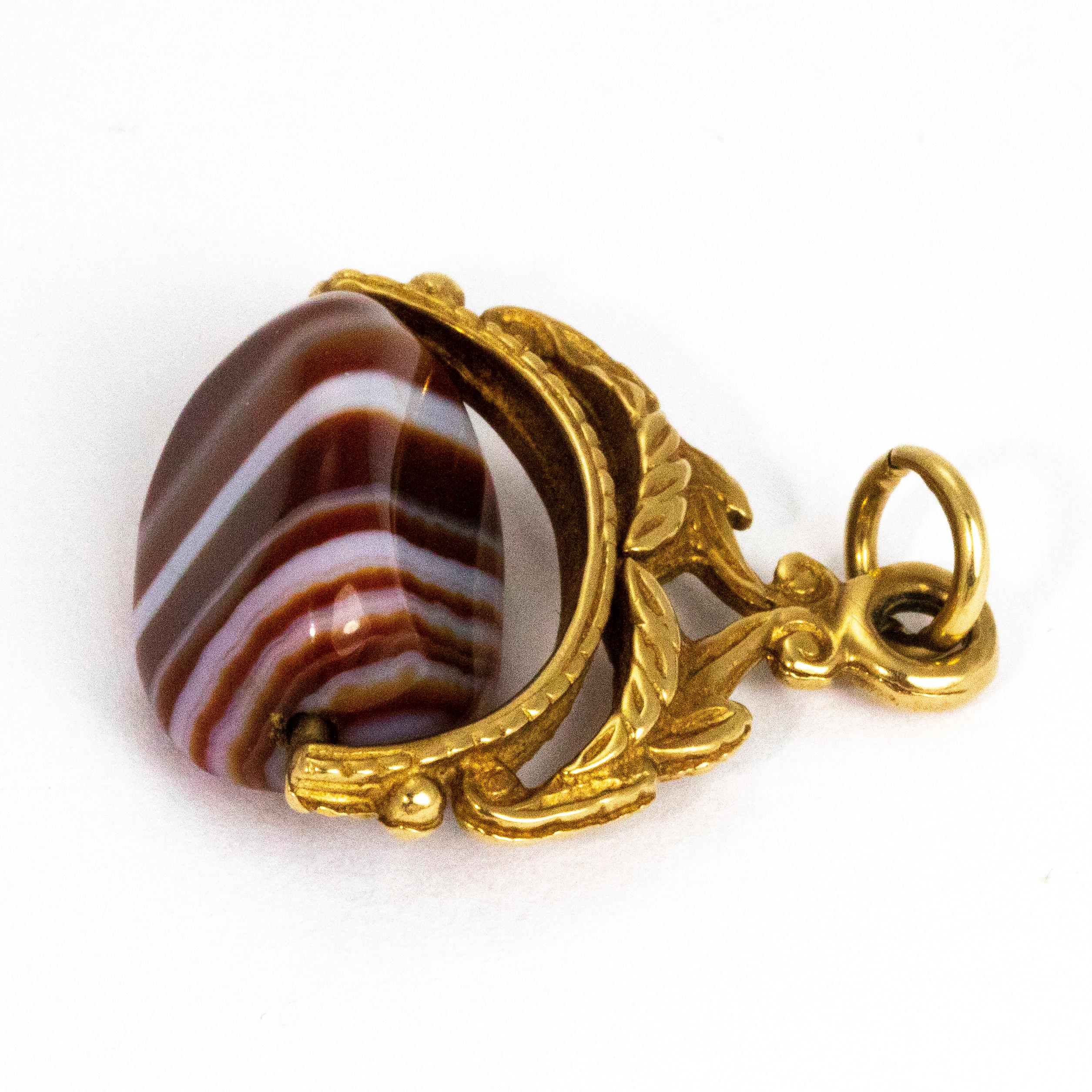 A swivel fob makes the perfect pendant that is sure to draw attention. This particular fob holds a stunning striped agate stone with deep rich reds and browns paired with white. The fob itself is modelled out of 9ct gold and features leaf and scroll