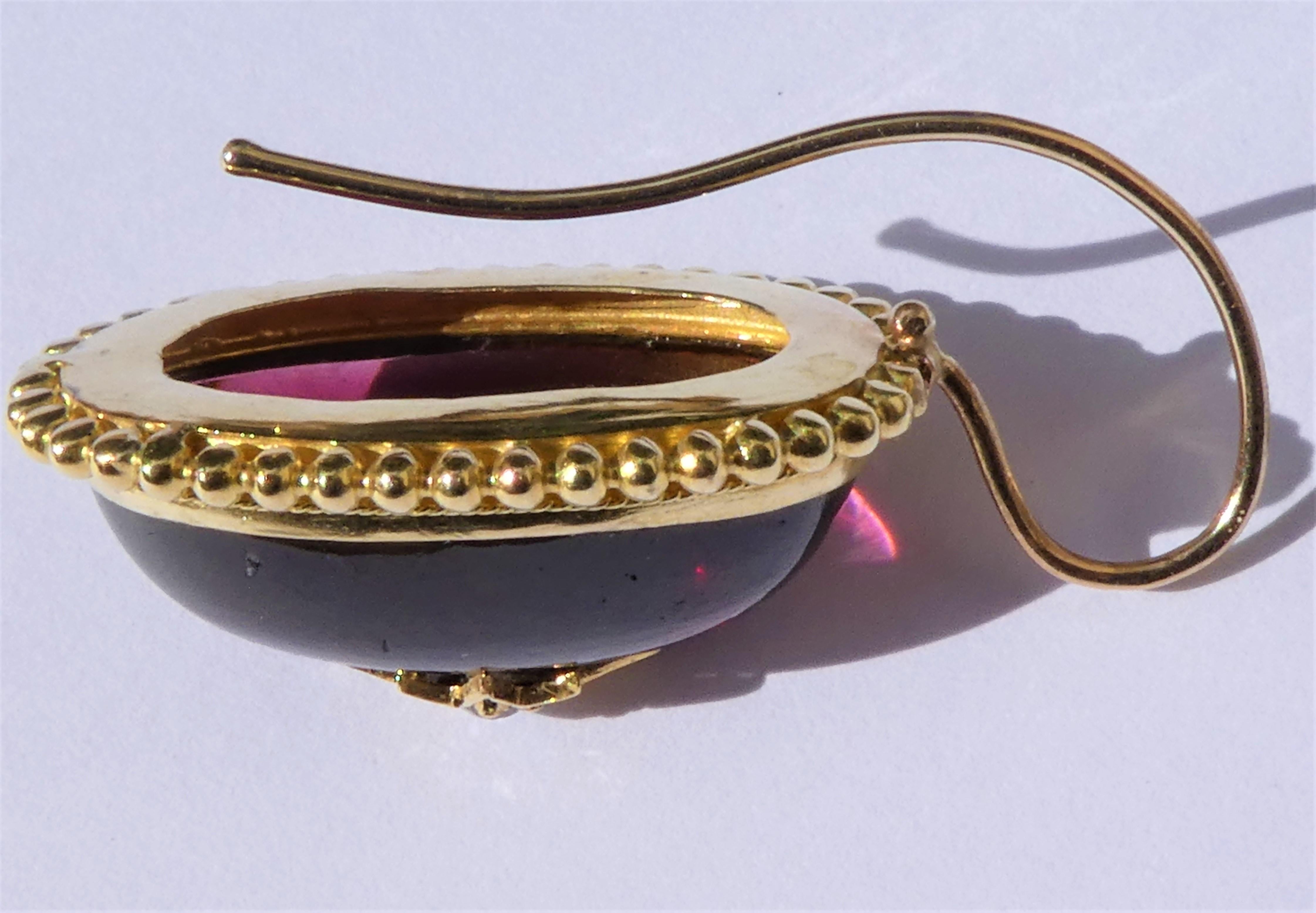 These lovely earrings date from the 1890s and are designed as red almandine garnet pendants surrounded by fine 14 karat yellow gold granulation. The large oval almandine garnets in cabochon cut have a hollowed out back allowing light to shine
