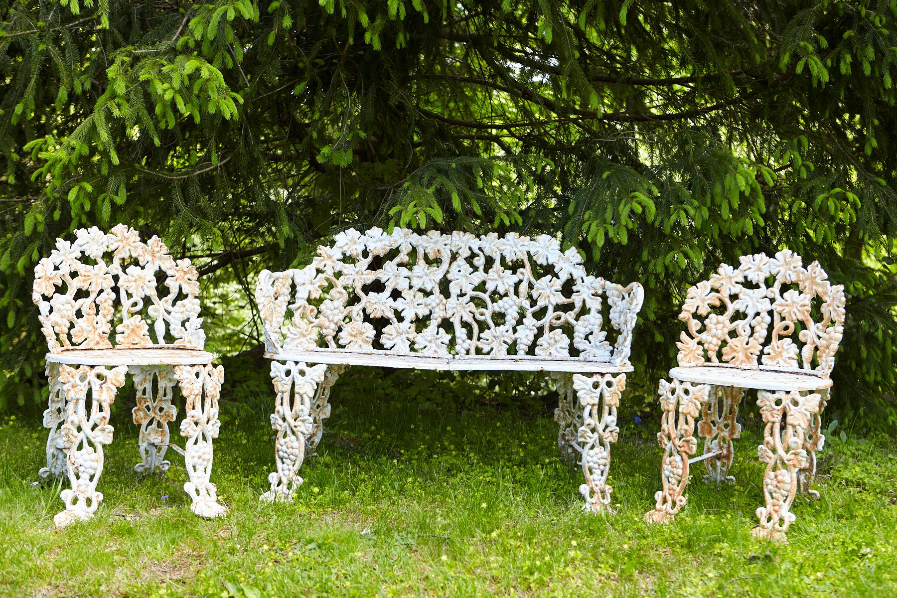 Heavy-duty white painted cast iron garden set, composed of a curved bench and two chairs with berry, leaf, and vine motifs. Bench, and chairs have some rust and moss area, which supports the lovely patina and wabi-sabi style look.
Bench: W 38 x D