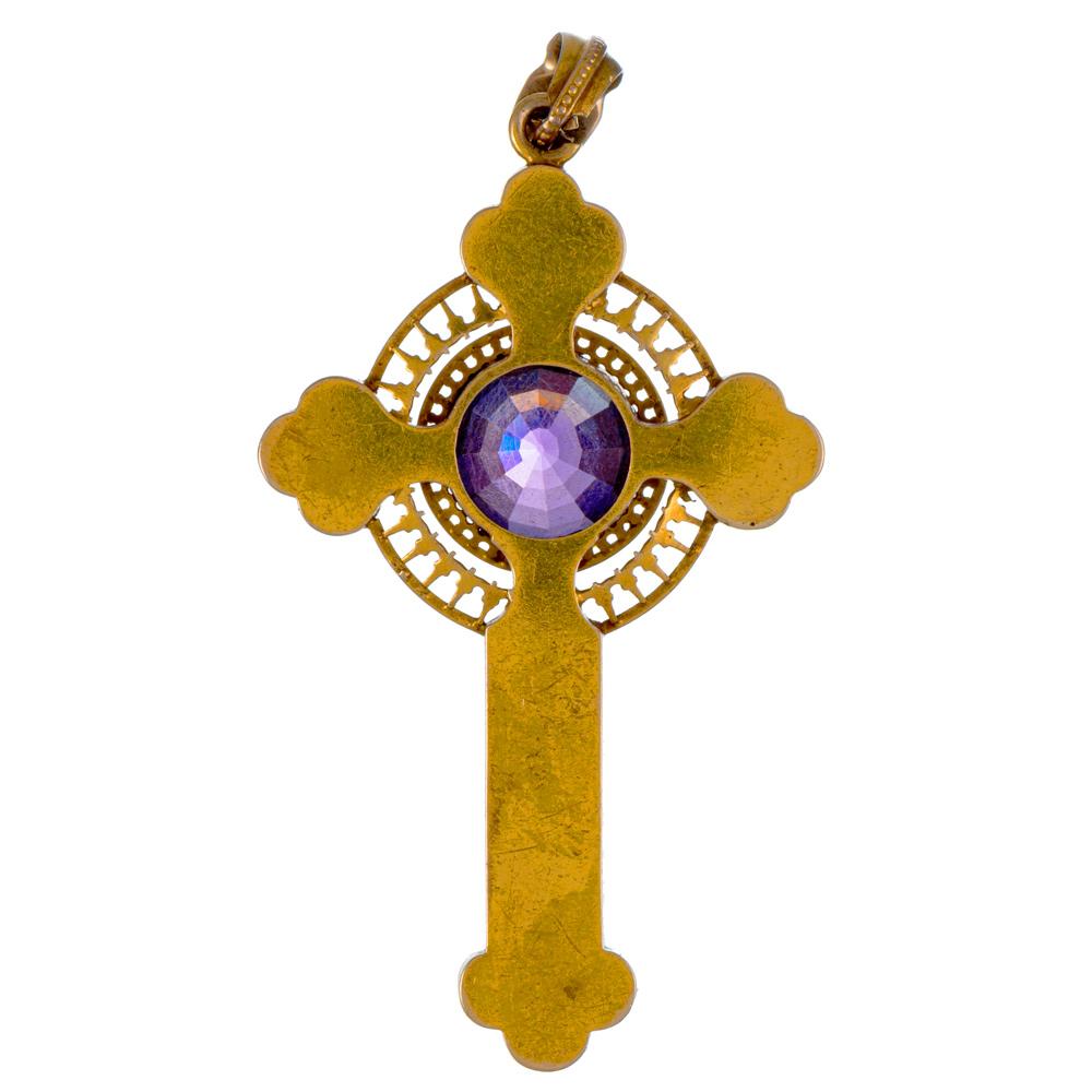 A glorious antique treasure for the devoted, the cross is rendered in 15k yellow gold and boasts a large faceted center amethyst framed by an intricate mounting of white enamel set upon a golden backdrop. The pendant measures 2.75 by 1.5 inches and