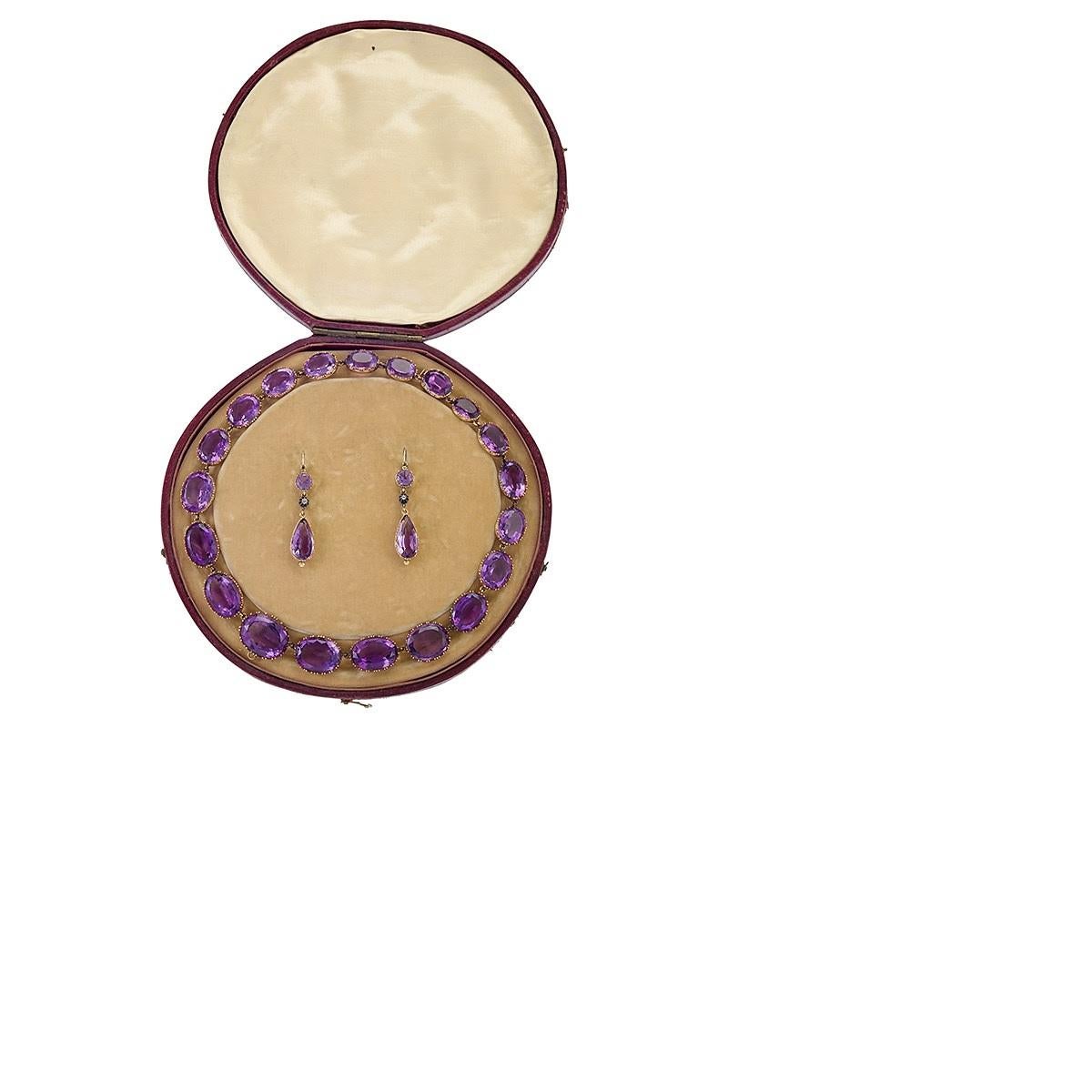 Eine englische viktorianische 18 Karat Gold und Amethyst Parure einer Rivière Halskette und Tropfen Ohrringe. Die Rivière besteht aus 20 tief gefärbten ovalen Amethysten in horizontaler Ausrichtung, die in zarte Tortenkrusten eingefasst sind und ein