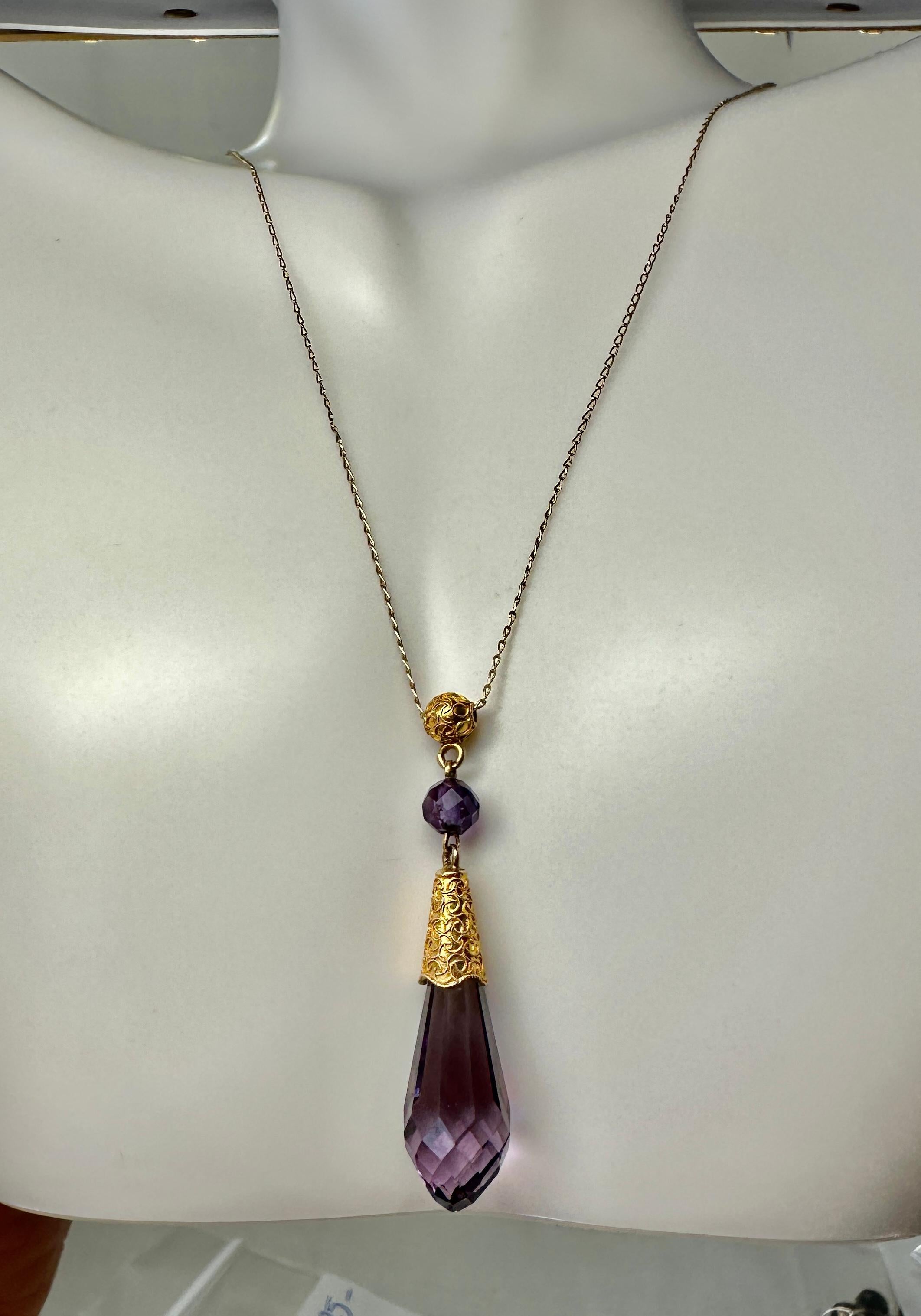 THIS IS A STUNNING ANTIQUE AMETHYST VICTORIAN ETRUSCAN REVIVAL 10-14 KARAT GOLD PENDANT NECKLACE.
The exquisite necklace has a briolette faceted natural amethyst drop with a finely decorated Etruscan hand applied bead and rope work accent surmount