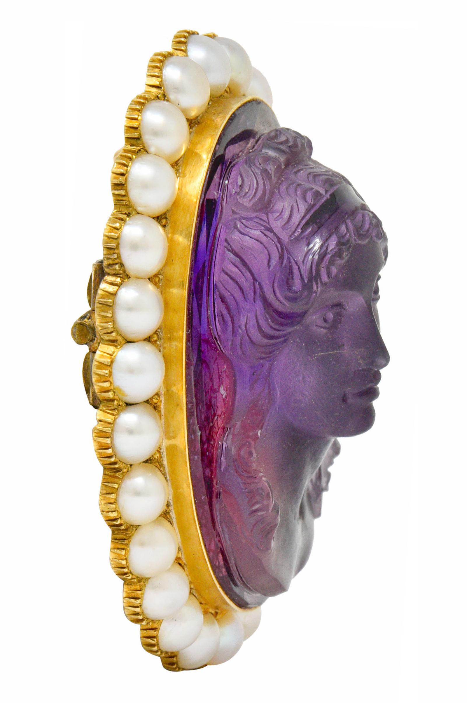 Centering an oval cut amethyst deeply carved to depict a front-facing woman with billowing hair

Transparent with a matte and gloss finish, deeply saturated purple in color

Surrounded by a halo of 3.5 mm pearls, very well matched cream in body