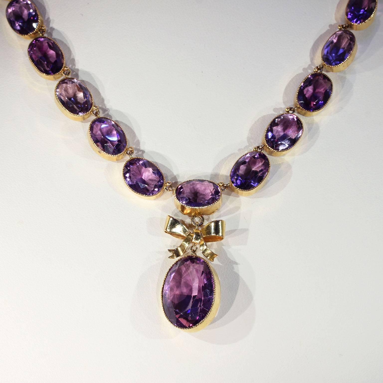 This antique Victorian amethyst gold necklace was handcrafted in England around 1900. It showcases 36 oval faceted amethysts set in 15 karat gold. The 35 stones around the neck are graduated and there is a large drop which hangs from a golden bow.
