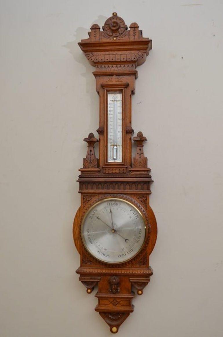 Sn181 Late Victorian aneroid barometer in oak, having brass bezel and bevelled glass with a centre setting hand, engraved and silvered dial and a fine and unusual blued steel indicator hand. The thermometer box has a bevelled glass with a flat bulb