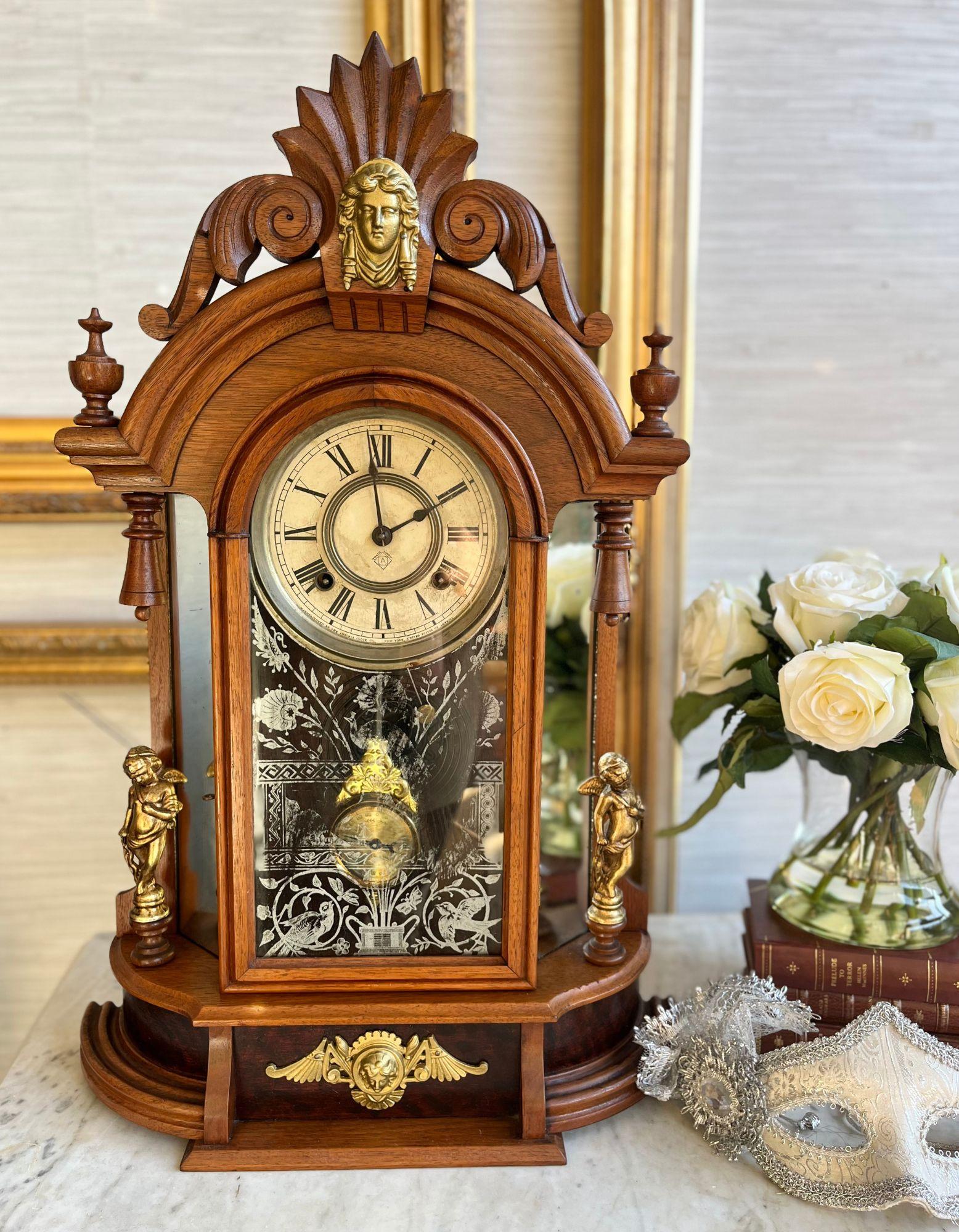 This exquisite antique mantel clock, crafted by the renowned Ansonia Clock Company in the 1800s, is a timeless piece of history and elegance. The clock features a beautifully carved wooden case adorned with intricate brass cherub sculptures on the