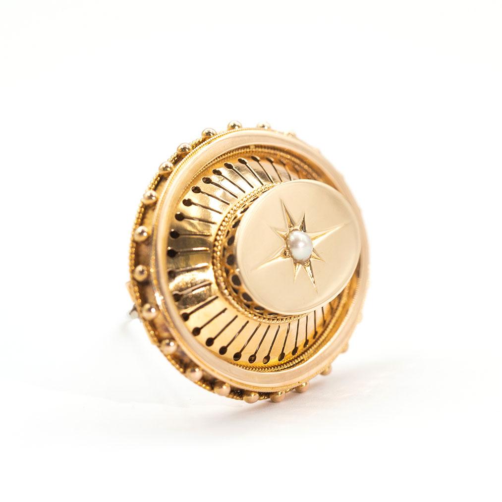 Carefully crafted in 18 yellow gold is this antique 19th century Victorian mourning brooch, her design details typical of this era.  She features a round white seed pearl delicately star bed set in a high dome top that flows down to an ornate border