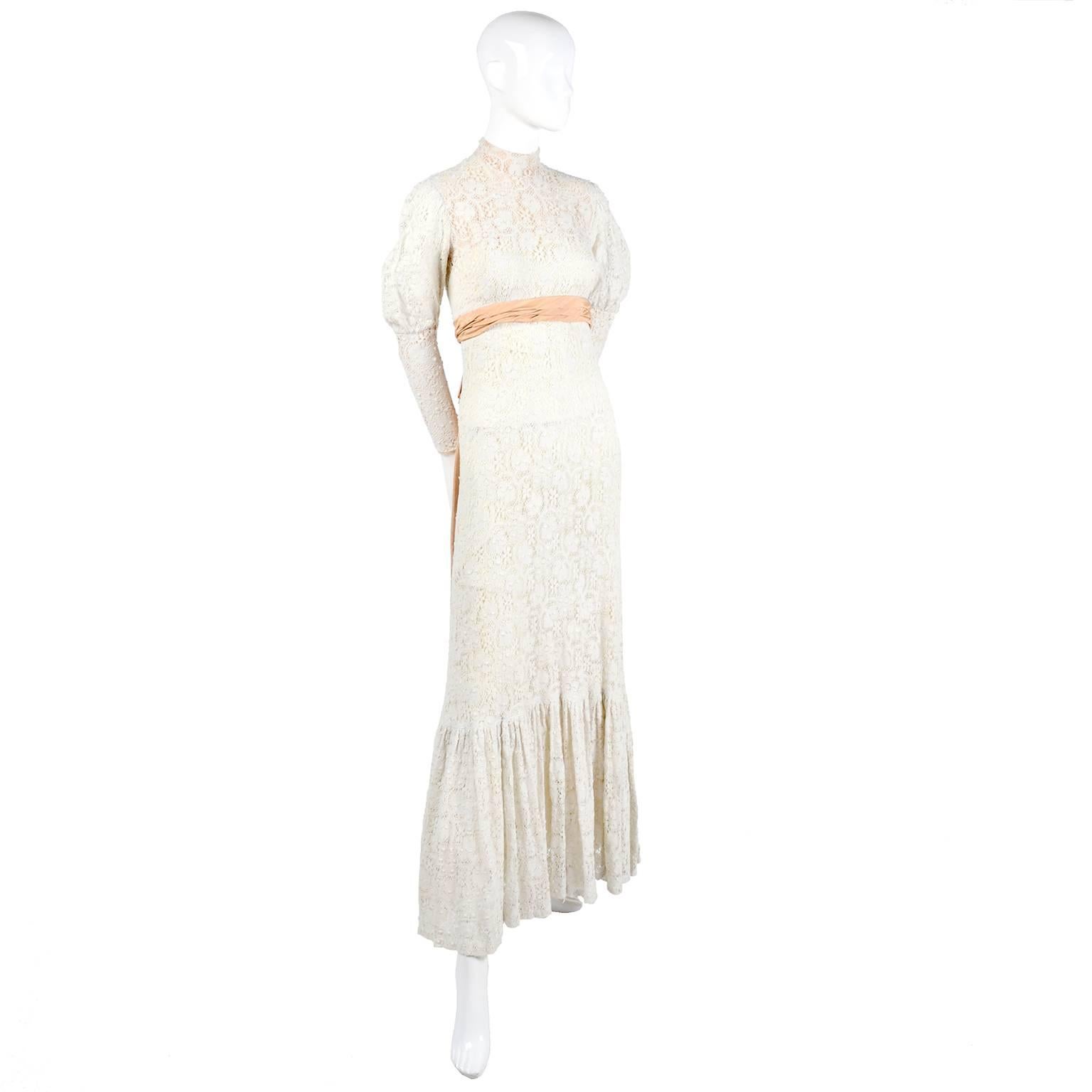 Este precioso vestido victoriano vintage de encaje es sencillamente exquisito, con su precioso dobladillo con volantes, escote de cuello alto y lazo de satén moaré melocotón en la espalda. Este fabuloso vestido vintage de encaje marfil podría