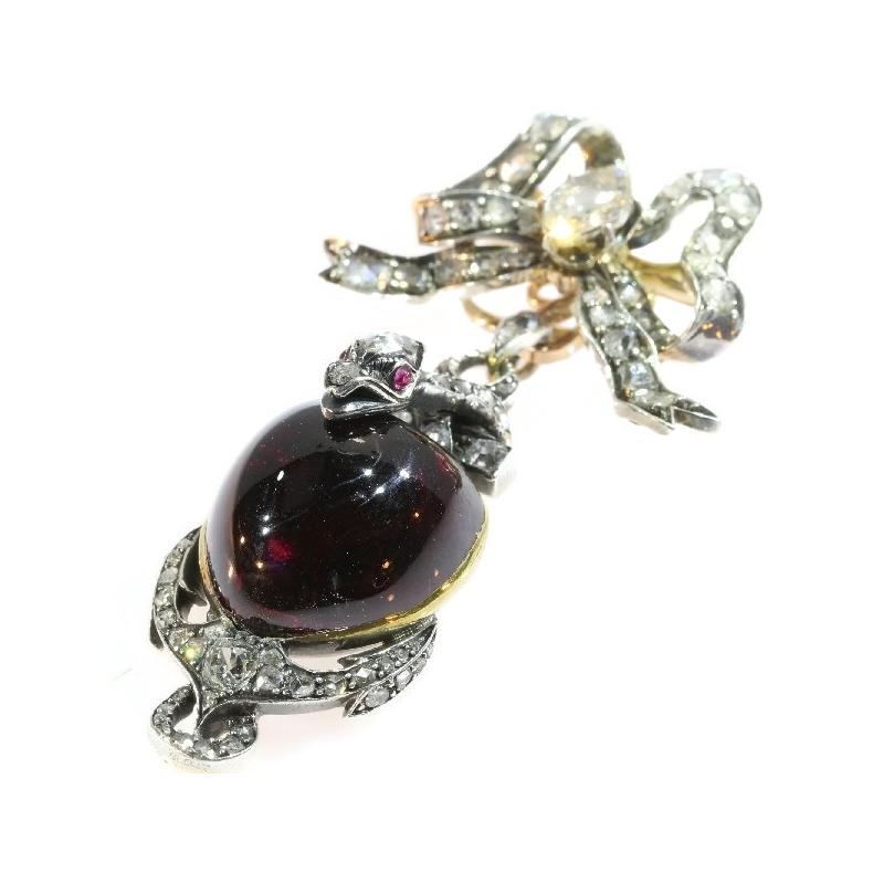 This Early-Victorian bi-colour gold-backed pendant from 1830 embodies a treasure of symbols through a deep pink garnet heart, a silver-topped bow, snake, cross and anchor encrusted with three European cut diamonds and with a total of 86 rose cut