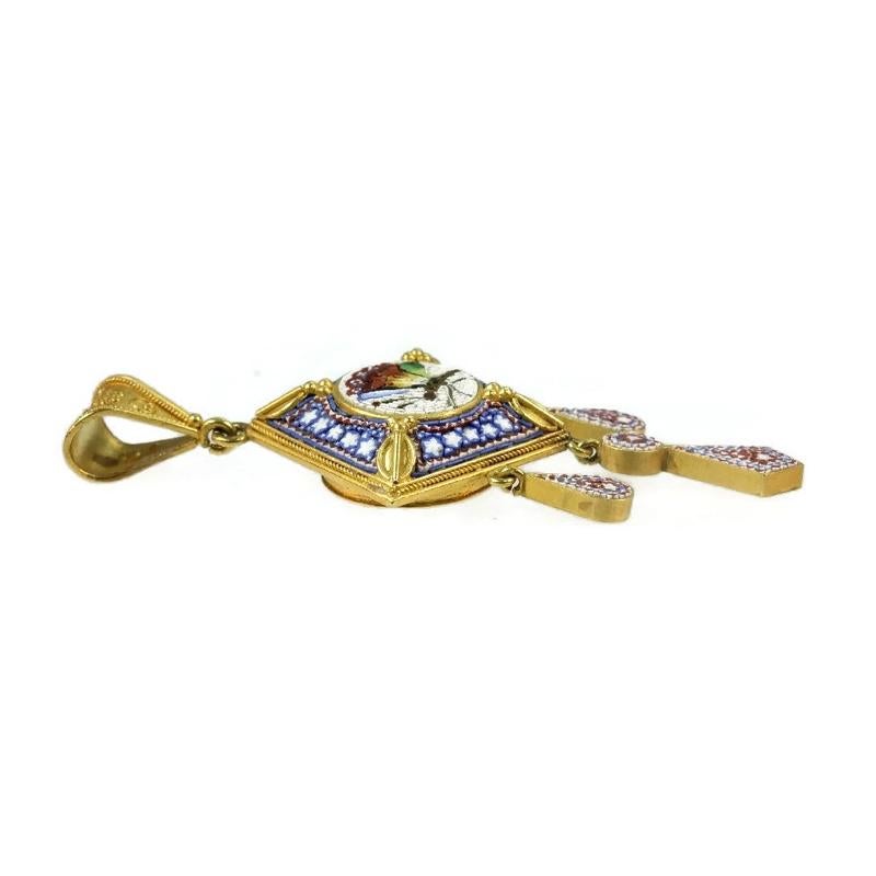 This square-shaped 18K yellow gold Victorian pendant depicts a mosaic butterfly with wings of blue, green and yellow to red glass inlay work on a white background. While the corners of the square have gold oval ornaments with granules, the borders