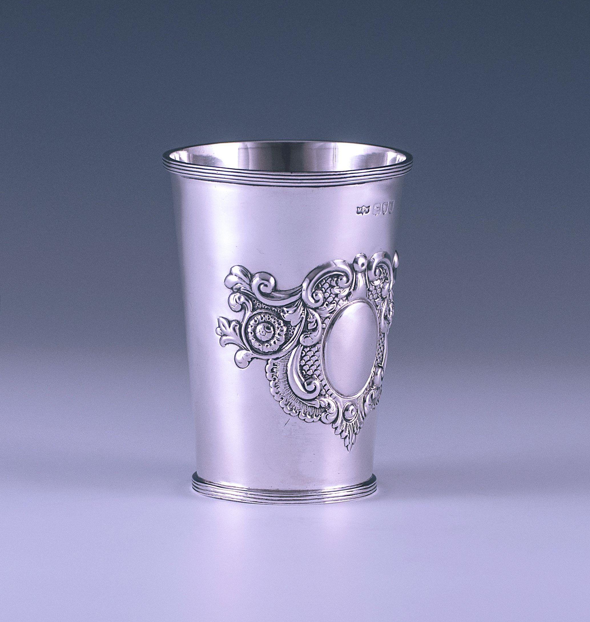 A stylish Victorian antique sterling silver beaker has a circular flared form onto a circular spreading foot. The surface of the beaker has a chasing scrolling leaf floral motif, in the centre of which is a plain cartouche. The top and base borders