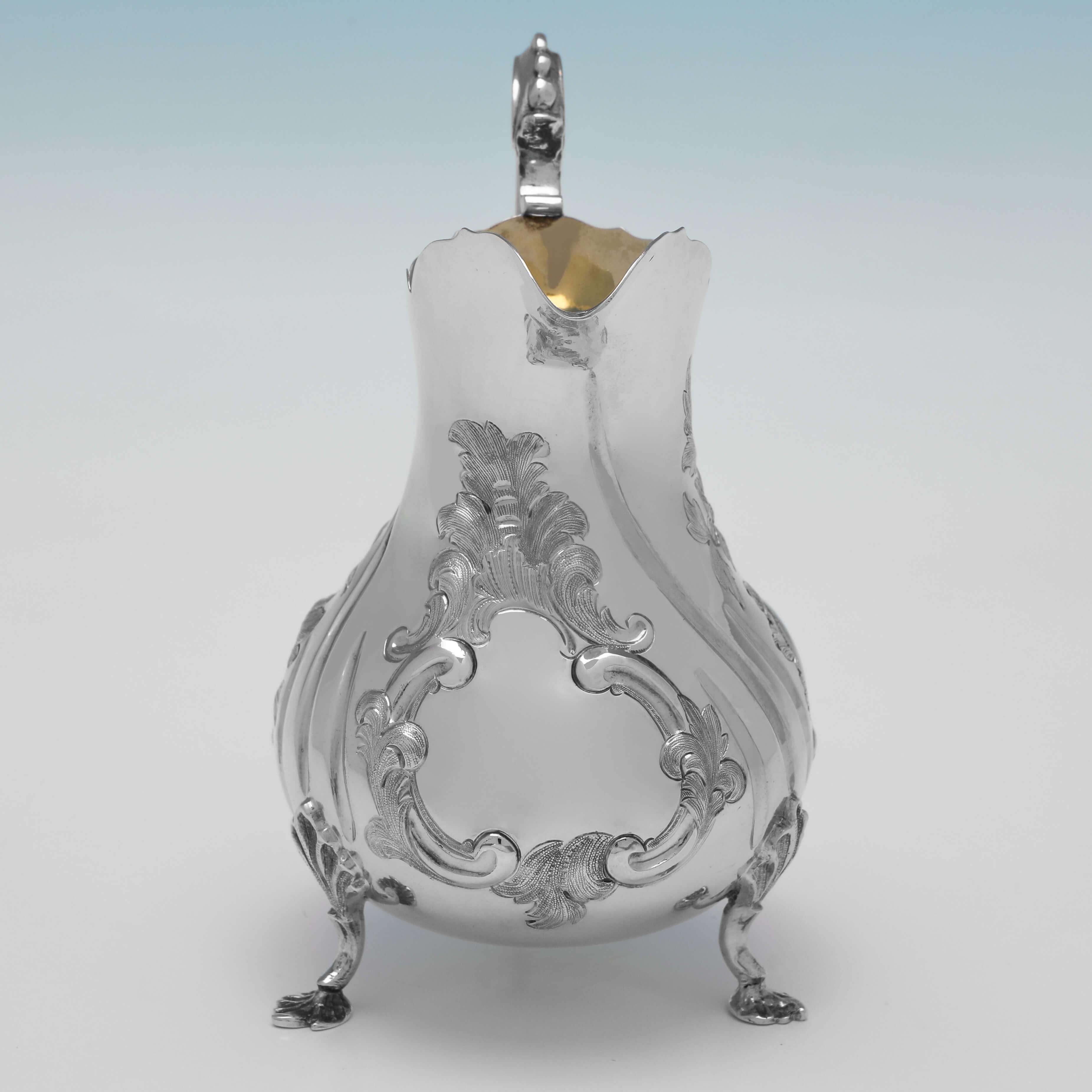 Hallmarked in London in 1856 by George John Richards, this very attractive, Victorian, Antique Sterling Silver Cream Jug, stands on three scroll feet, and features a gilt interior, and chased floral and scroll decoration to the body. 

The cream