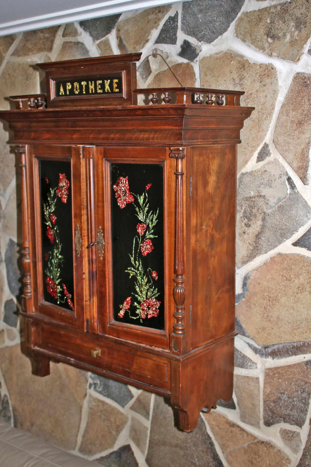 This is a beautiful Late Victorian apothecary cabinet. The letters are beautifully crafted from a gold hued foil, the flowers were crafted with the samew technique, but in green and red. The cabinet is in original condition.