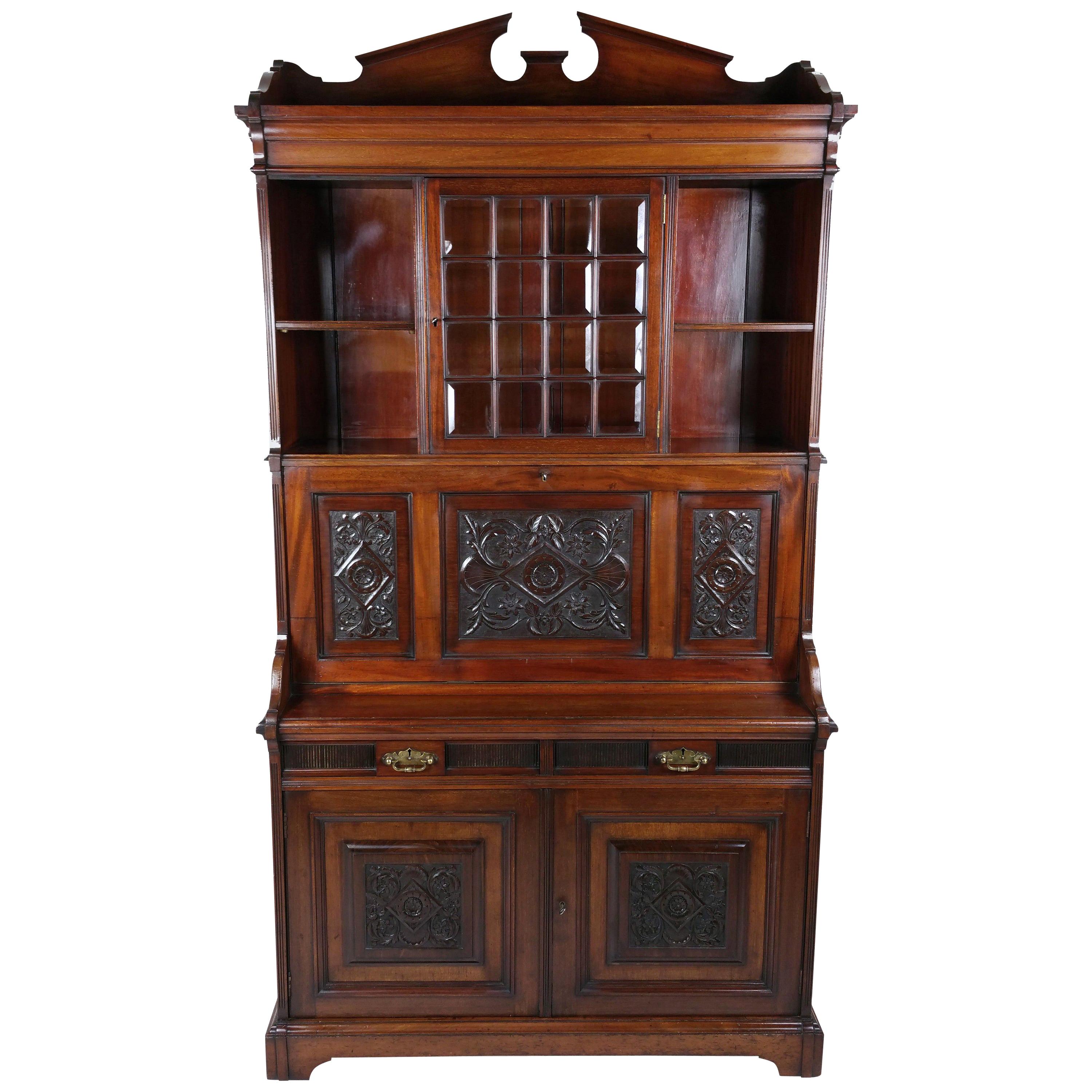 This outstanding and ornate Victorian Arts & Crafts walnut Secretaire cabinet features a central beveled glass door in between shelves on the top over a drop flap with a carved and fitted interior central space. The bottom half of the cabinet has