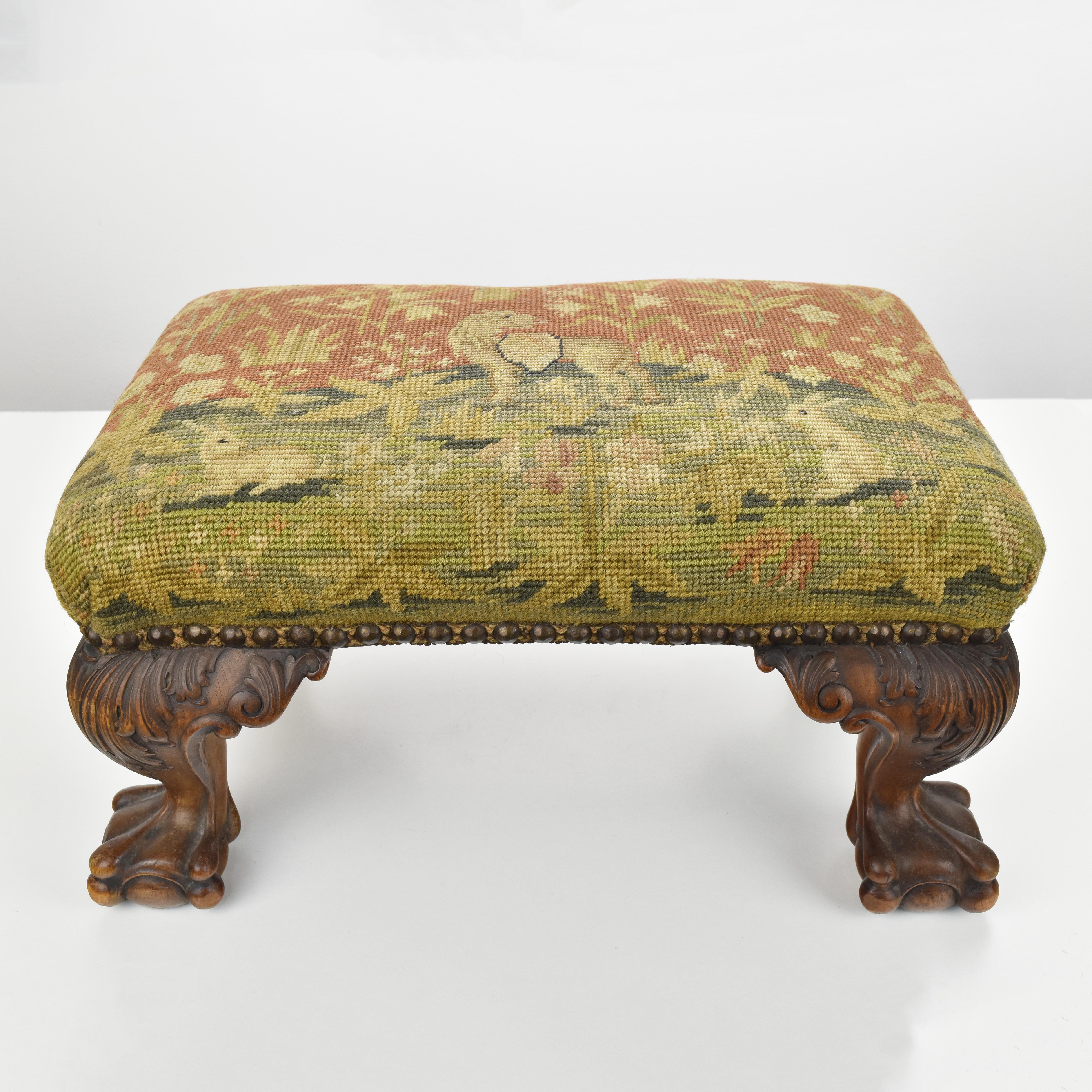 An antique early Victorian footstool with finely detailed hand-carved claw and ball feet made of walnut wood, upholstered with a rich ornated Aubusson tapestry with an heraldic lion in centre, two white rabbits and rich floral foliage.