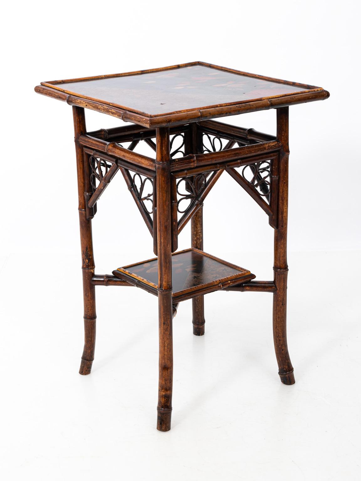 Victorian Aesthetic Movement style two-tier side table in bamboo, circa early 20th century. The painted tabletop is highlighted by Japonesque flowers and geometric shapes. Please note of wear consistent with age including wear to the bamboo frame.