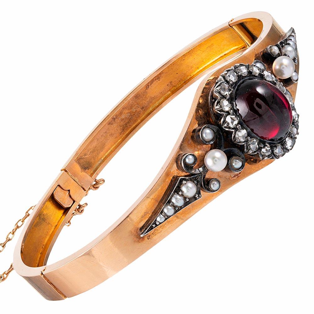 A lovely Victorian creation, rendered in 18 karat rose gold, the design is centered upon a cabochon garnet and rose cut diamond cluster, flanked by an ornate display of pearls. The oval-shaped bangle opens with a double set of hinges and is secured